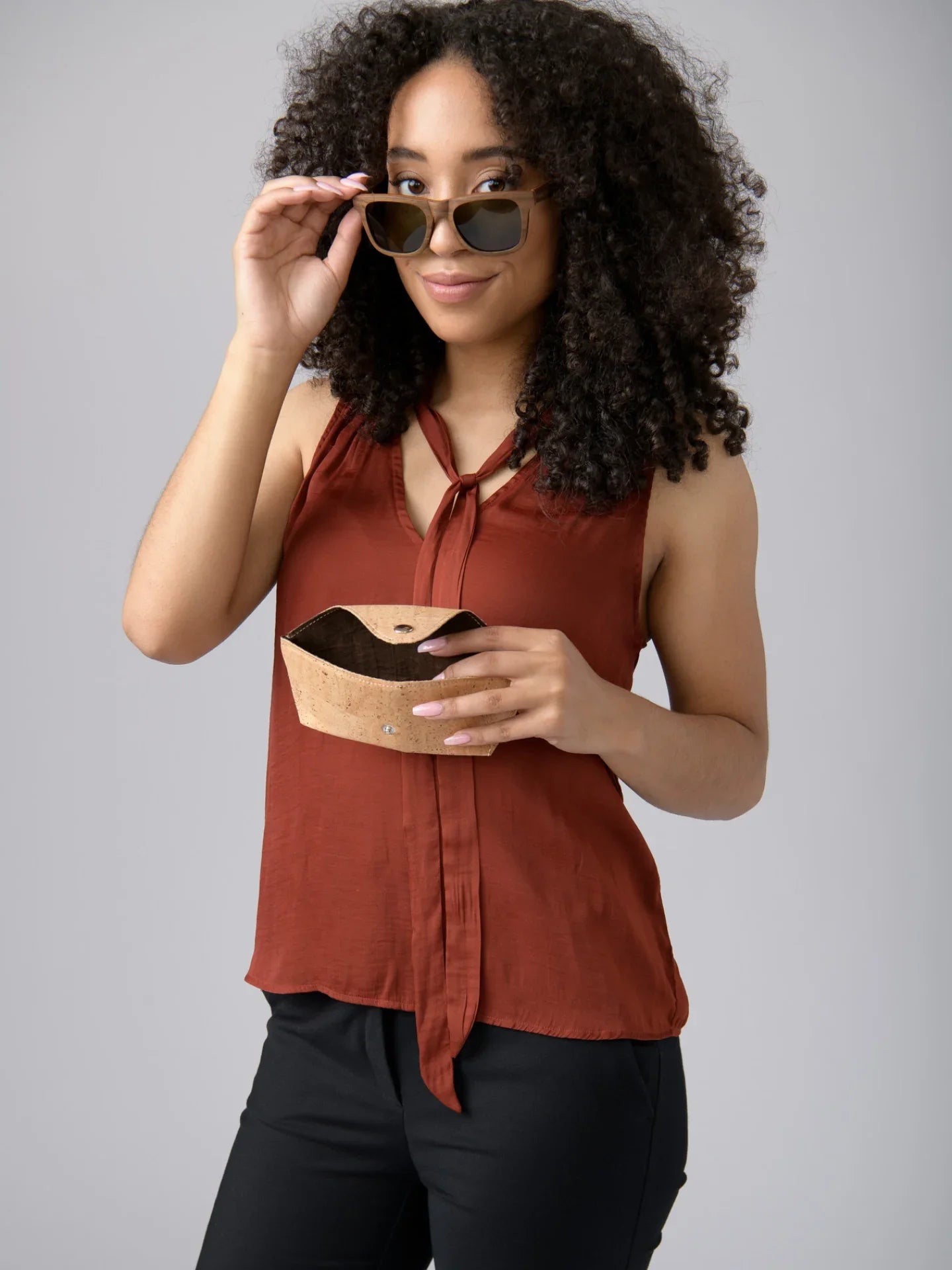 Woman in rust sleeveless top wearing sunglasses, holding cork case, Qu!rk Boutique style