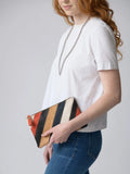 Woman holding striped cork clutch, wearing a white shirt and silver chain at Qu!rk Boutique
