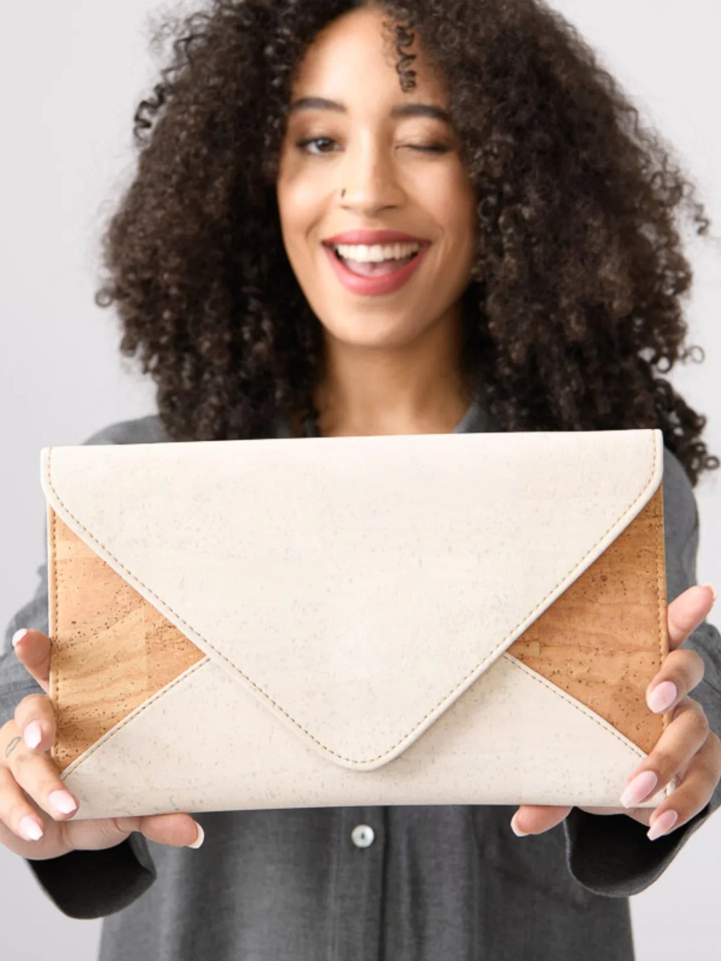 Woman holding eco-friendly cork and cream envelope clutch, smiling, at Qu!rk Boutique
