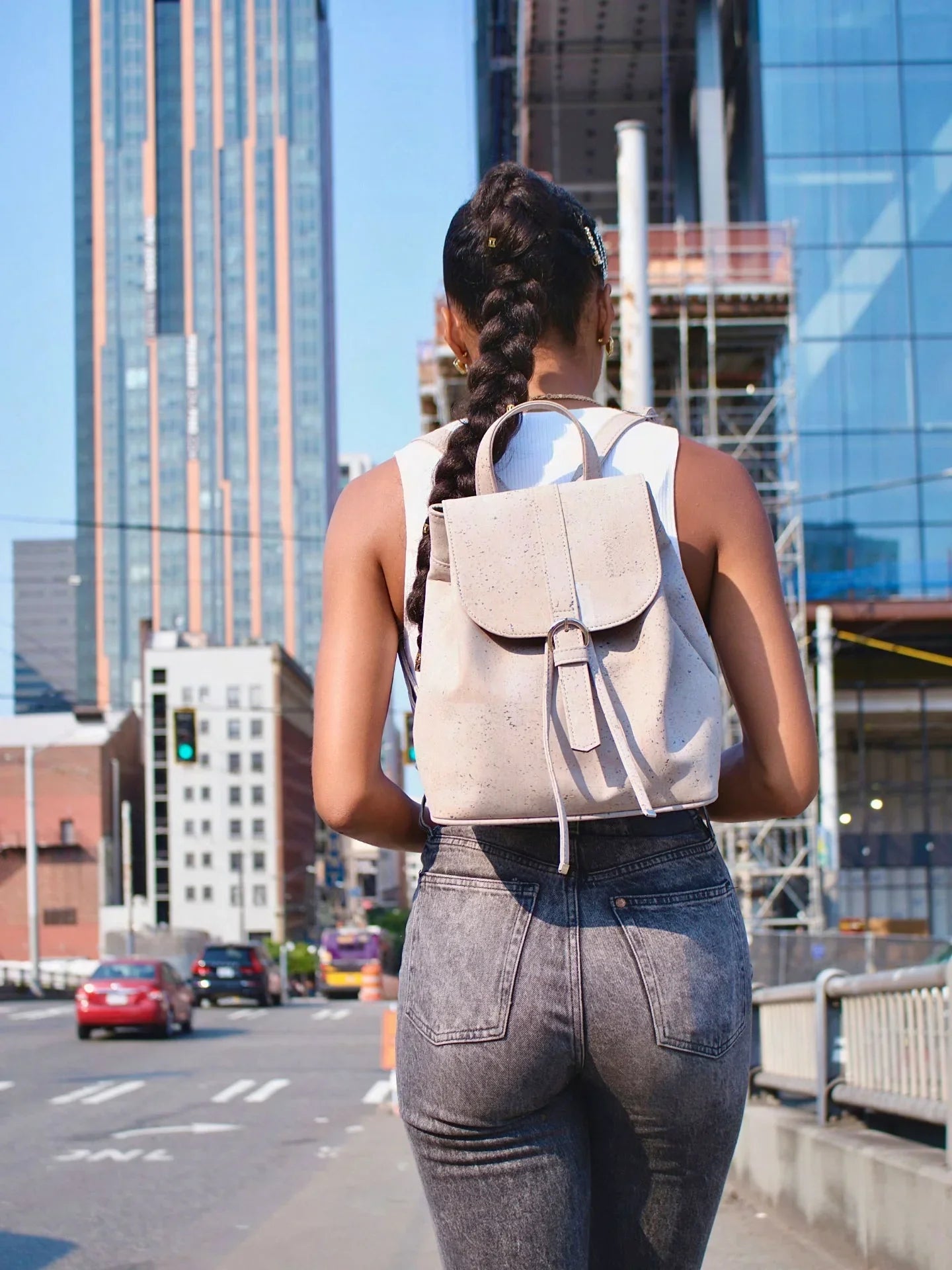 Woman with long braid wearing grey jeans and a speckled sustainable backpack in urban cityscape