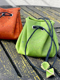 Green and orange cork drawstring pouches on an outdoor wooden table, Qu!rk Boutique gifts