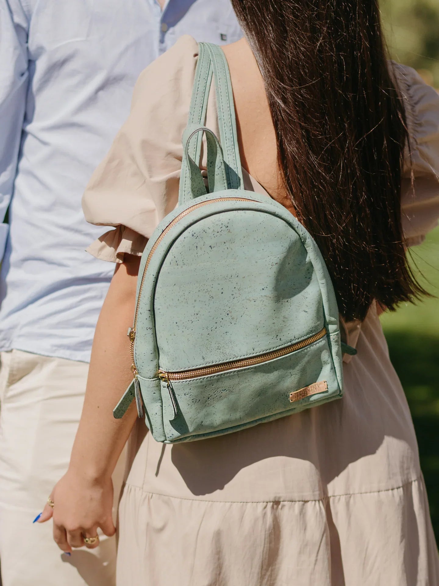 Woman wearing light green eco-friendly backpack from Qu!rk Boutique, outdoors in sunlight.