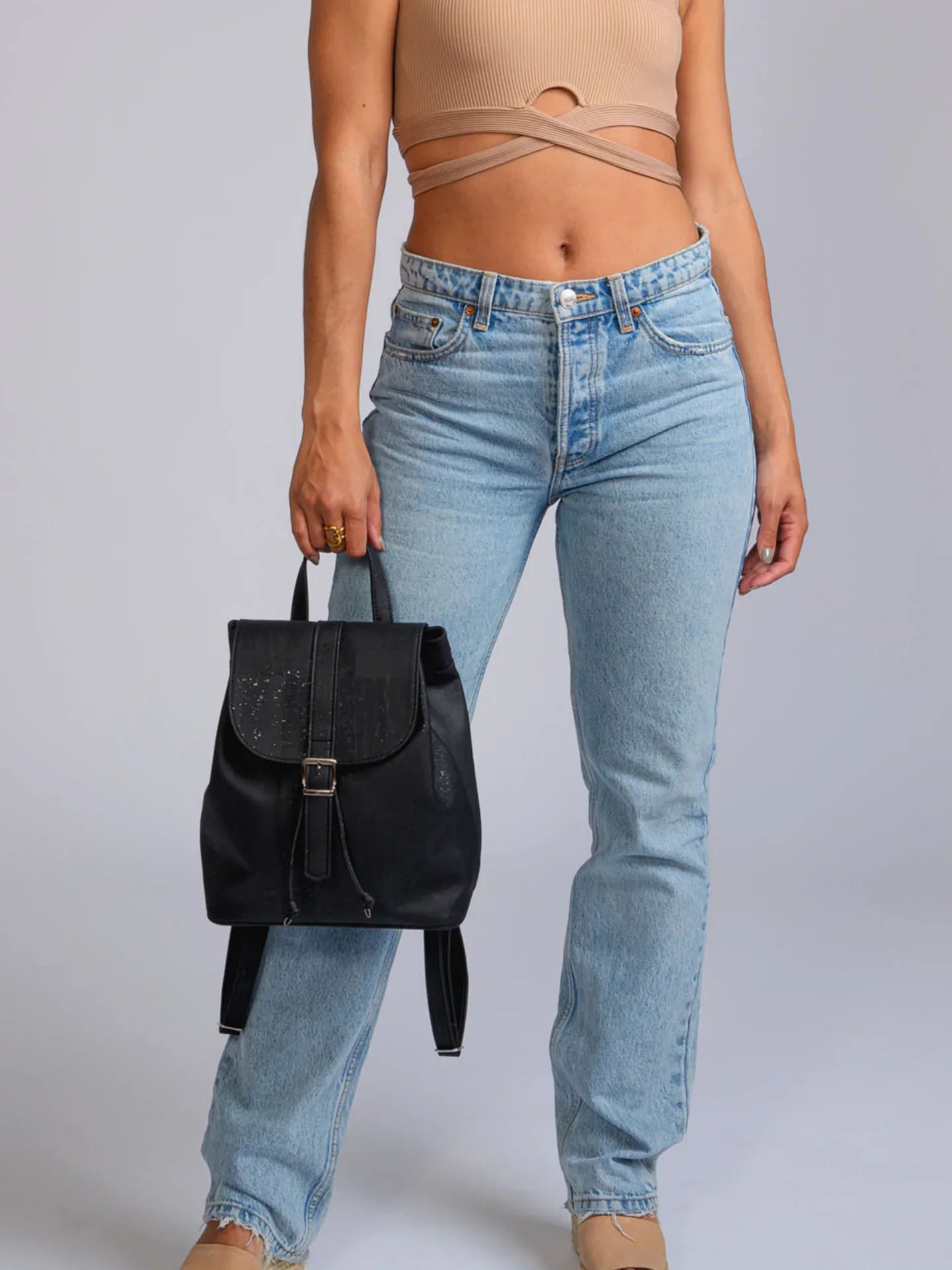 Woman in light denim jeans and beige crop top holding a black backpack, Qu!rk Boutique style