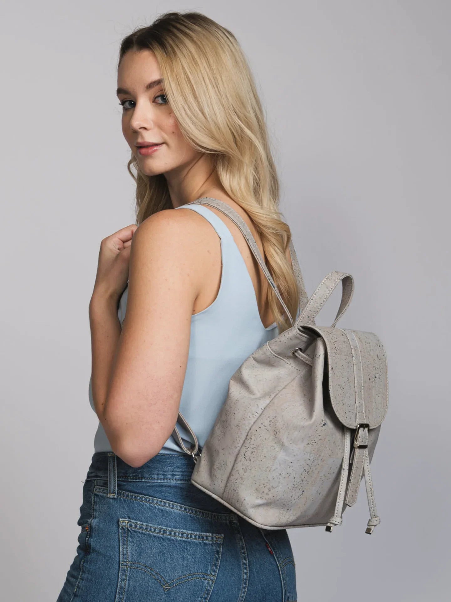 Woman wearing light blue top, denim jeans, and a sustainable grey backpack, Qu!rk Boutique