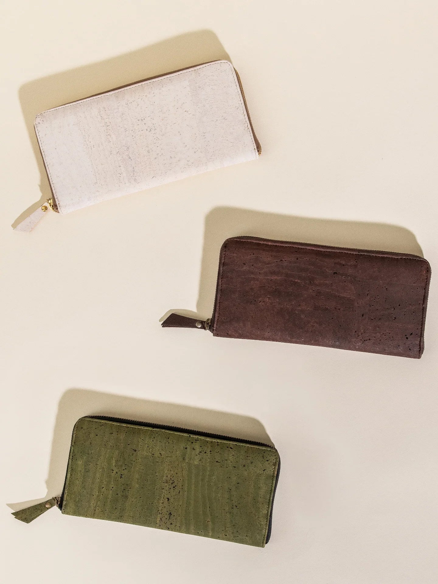 Three sustainable zip wallets in cream, brown, and green on a neutral backdrop at Qu!rk Boutique
