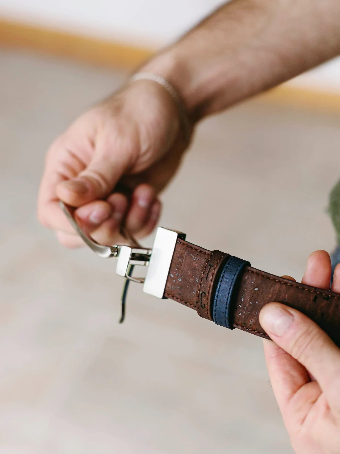 Hands holding a brown cork belt with silver buckle, eco-friendly accessory from Qu!rk Boutique