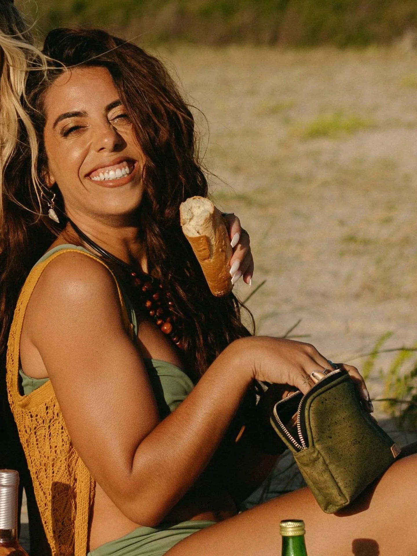 Smiling woman in green swimsuit with sustainable bag and baguette at sunny beach picnic