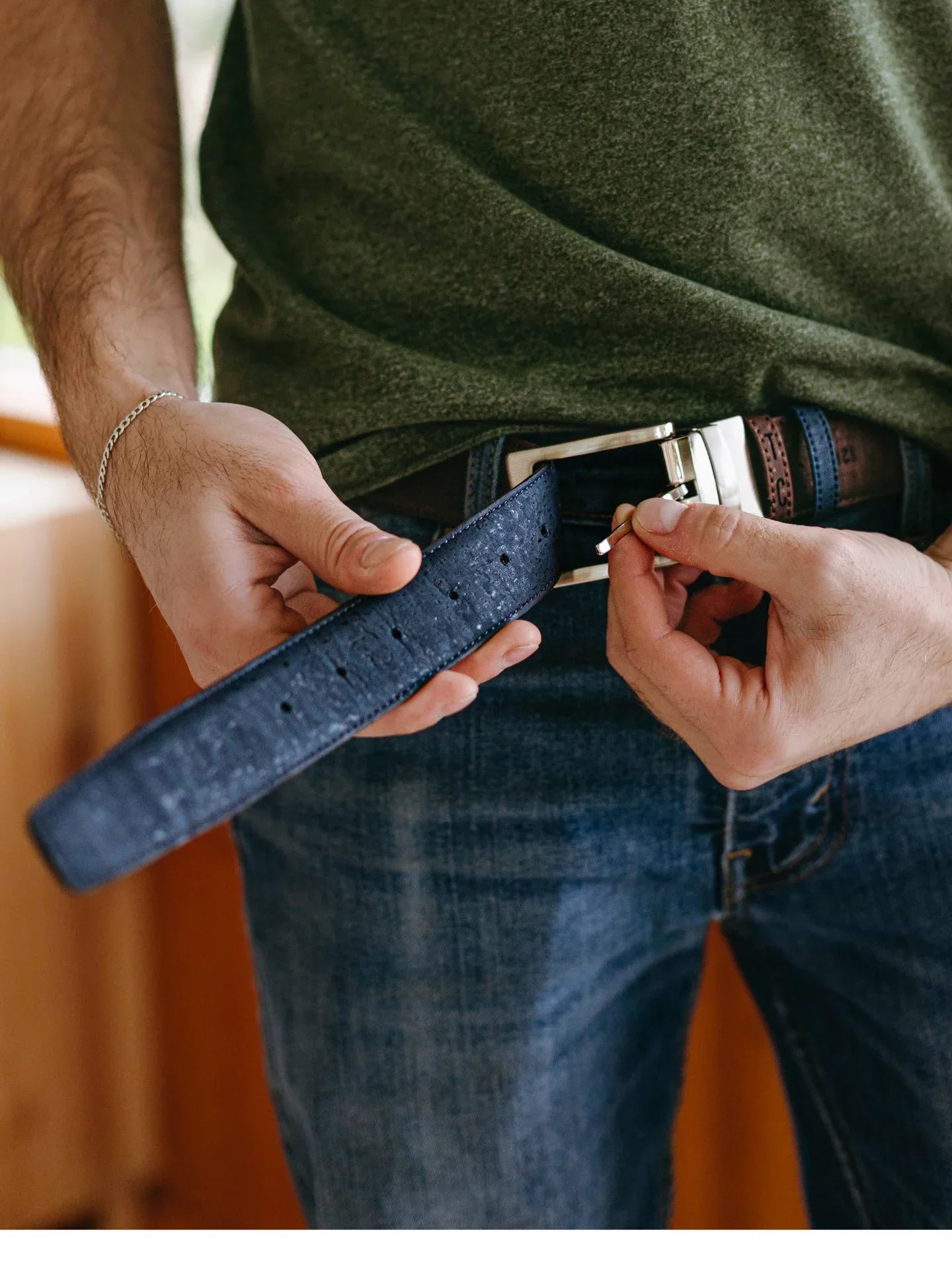 Person wearing jeans and a green shirt fastening a blue textured belt