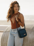 Woman in rust top and jeans with blue crossbody bag, outdoor fashion at Qu!rk Boutique