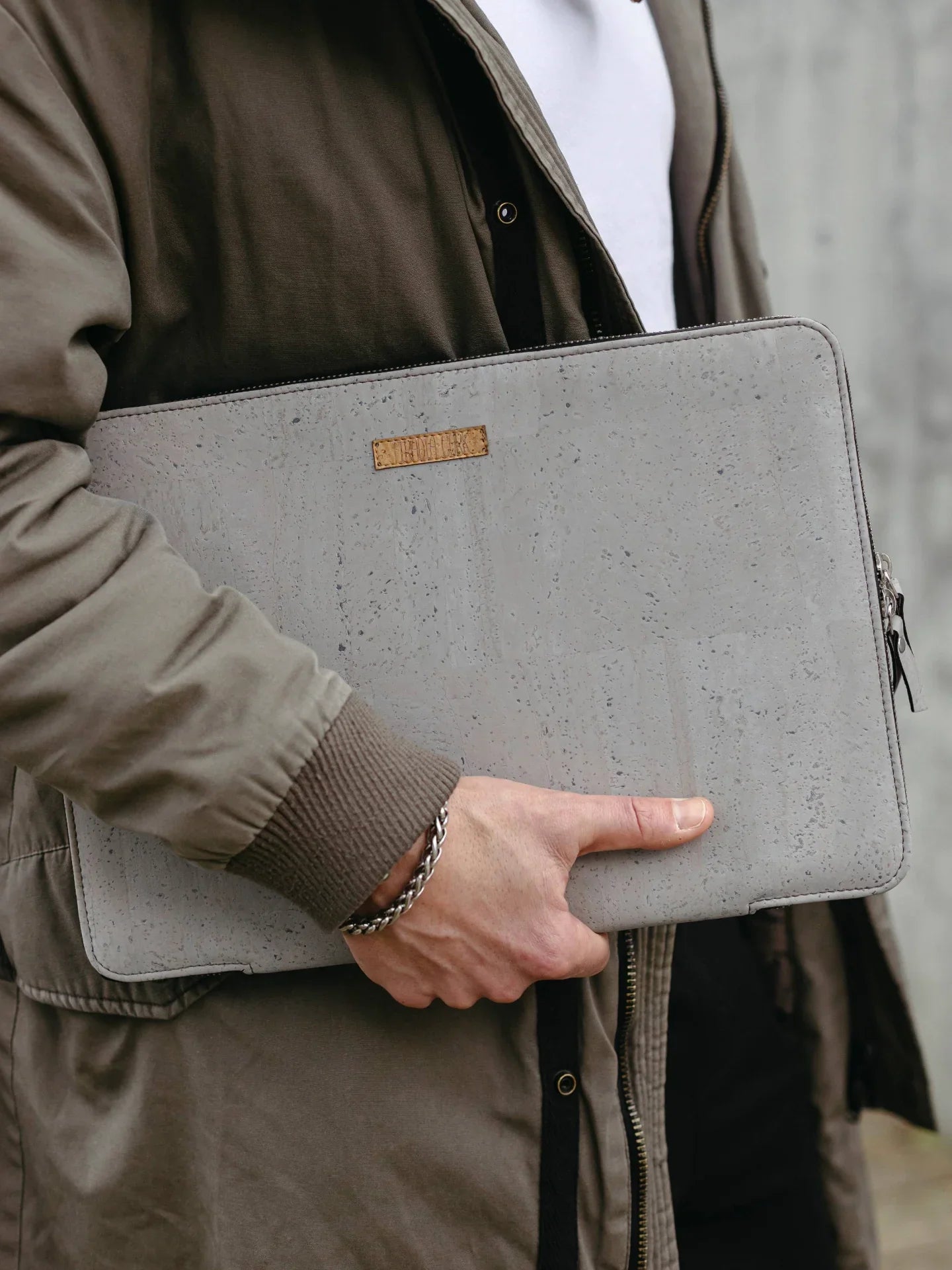 Person in olive jacket holding eco-friendly cork laptop sleeve from Qu!rk Boutique