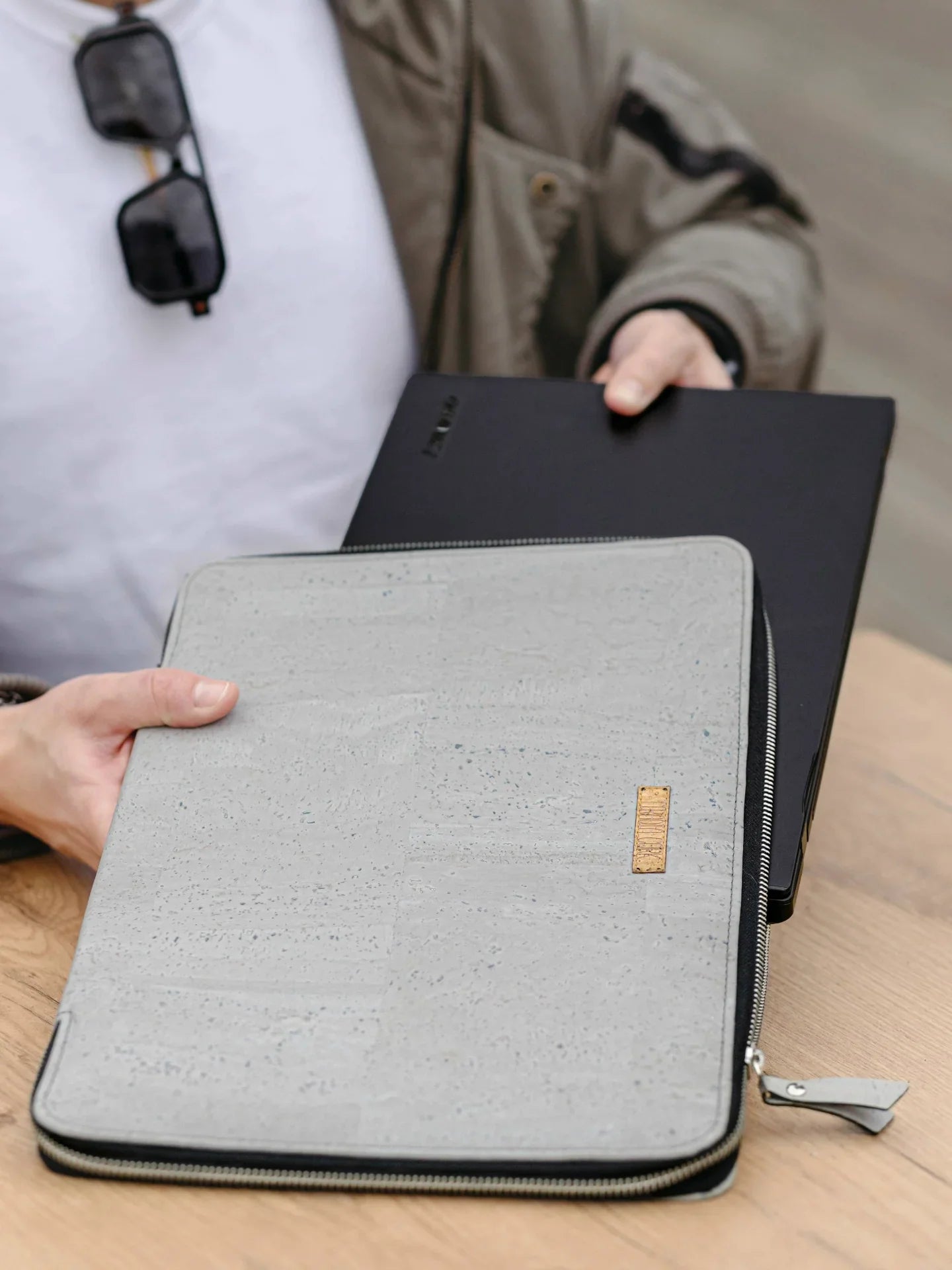 Person holding a grey cork laptop sleeve and black tablet on a wooden table at Qu!rk Boutique