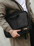 Person in taupe coat holding a sleek black vegan leather laptop bag from Qu!rk Boutique