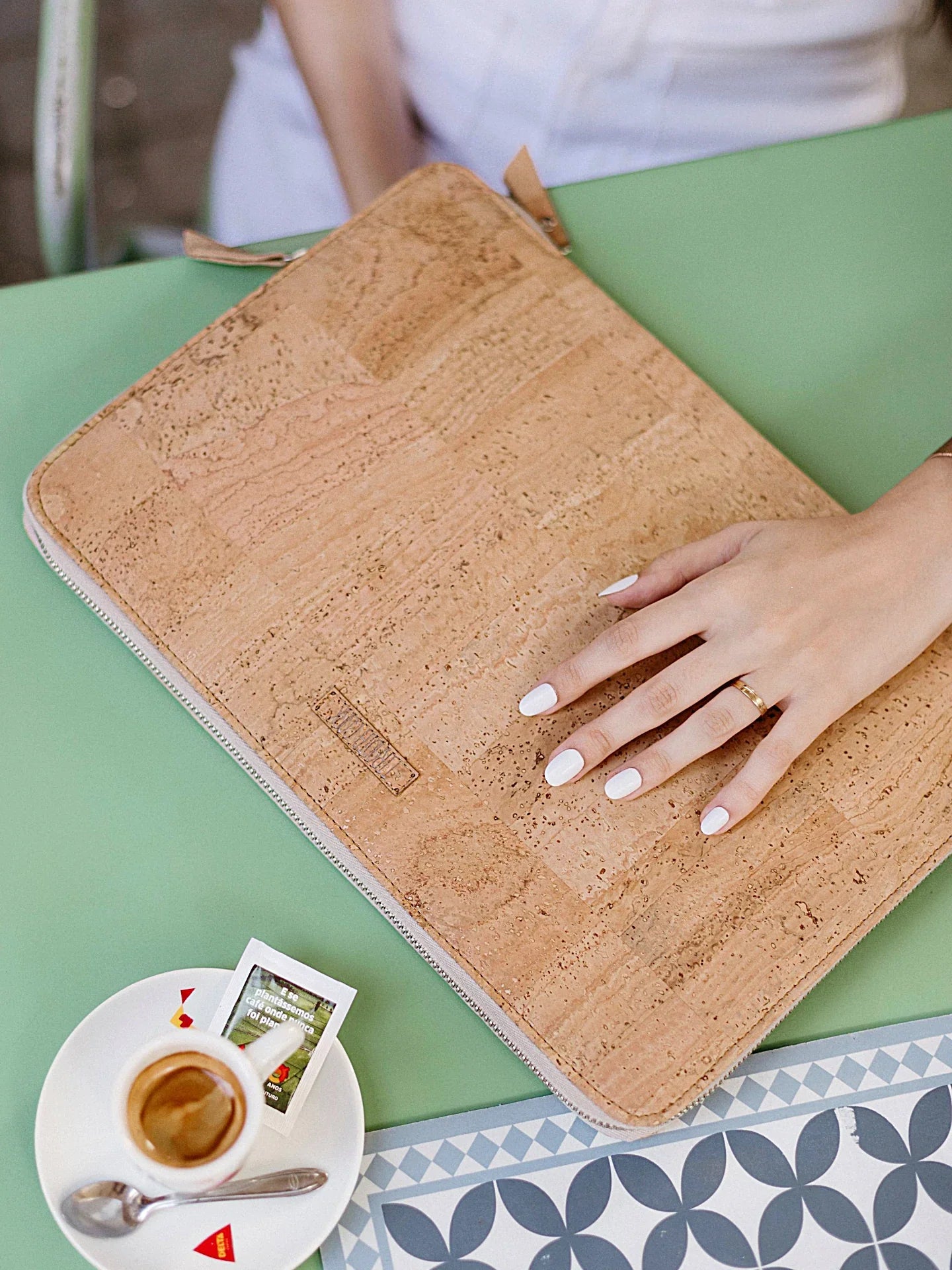 Woman’s hand on eco-friendly cork laptop sleeve with coffee at Qu!rk Boutique table
