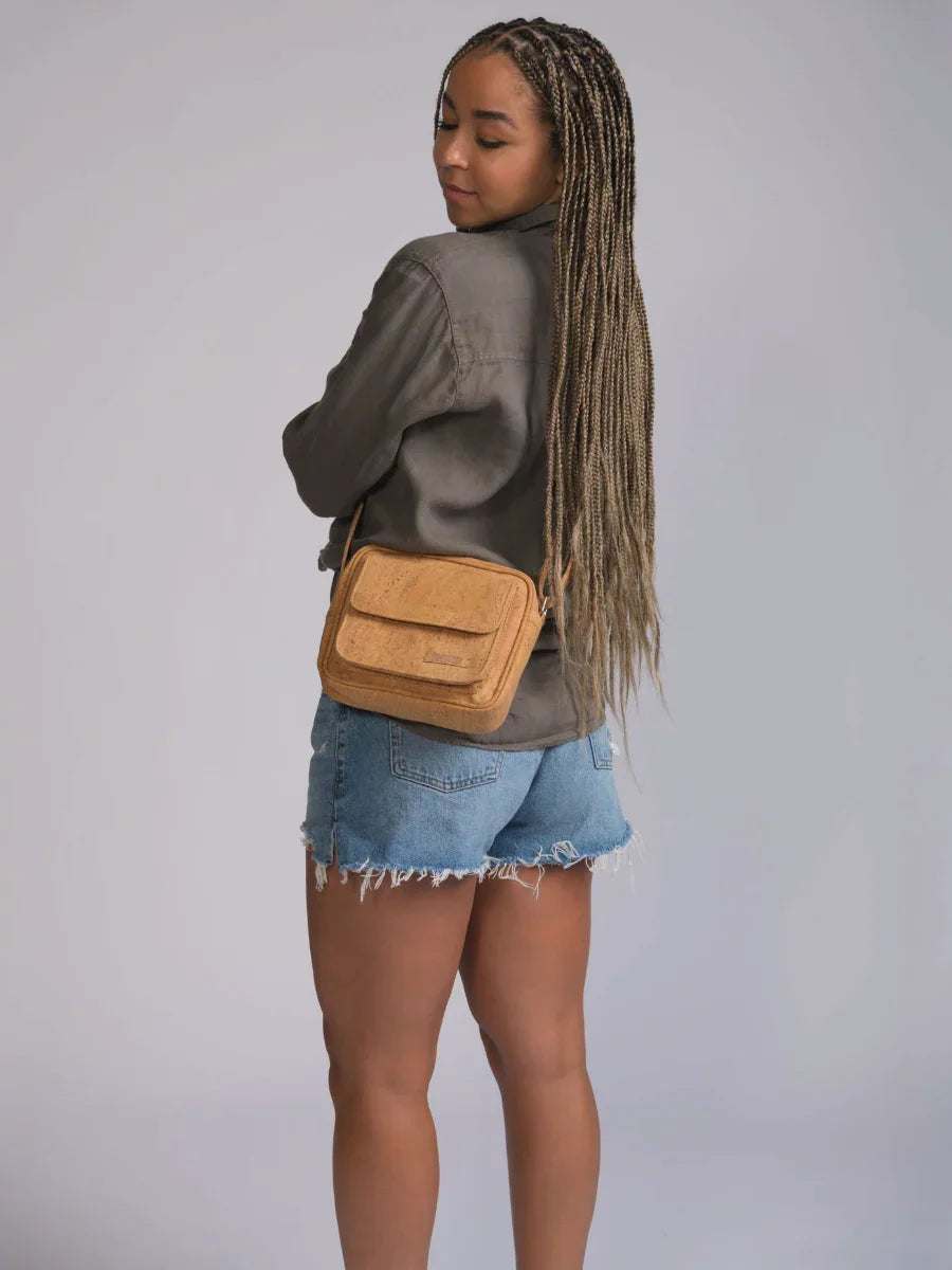 Woman in denim shorts and khaki jacket models a small tan crossbody bag, Qu!rk Boutique style