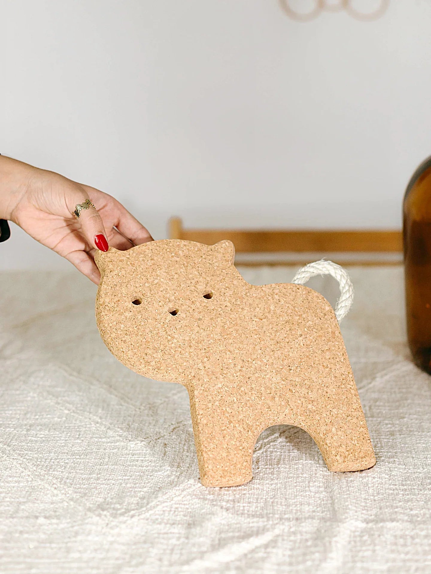 Hand holding cork animal-shaped decor with rope tail on textured table at Qu!rk Boutique