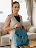 Woman in cozy boutique setting holding a blue sustainable cork backpack, Qu!rk Boutique style