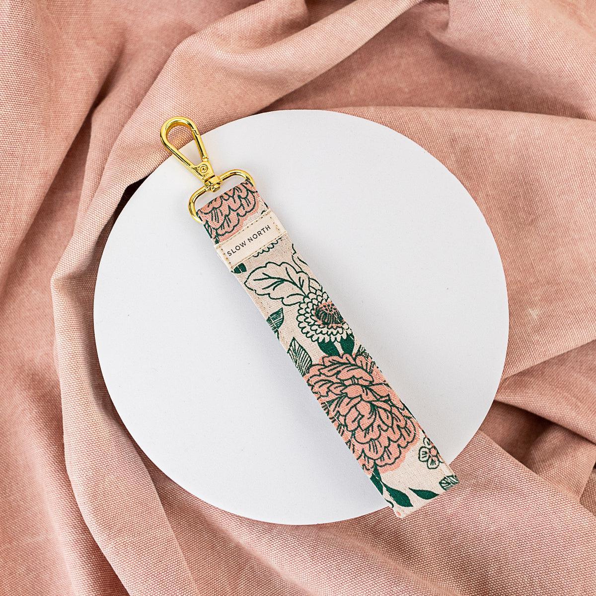 Floral fabric wristlet keychain with gold clasp on white plate and pink fabric background