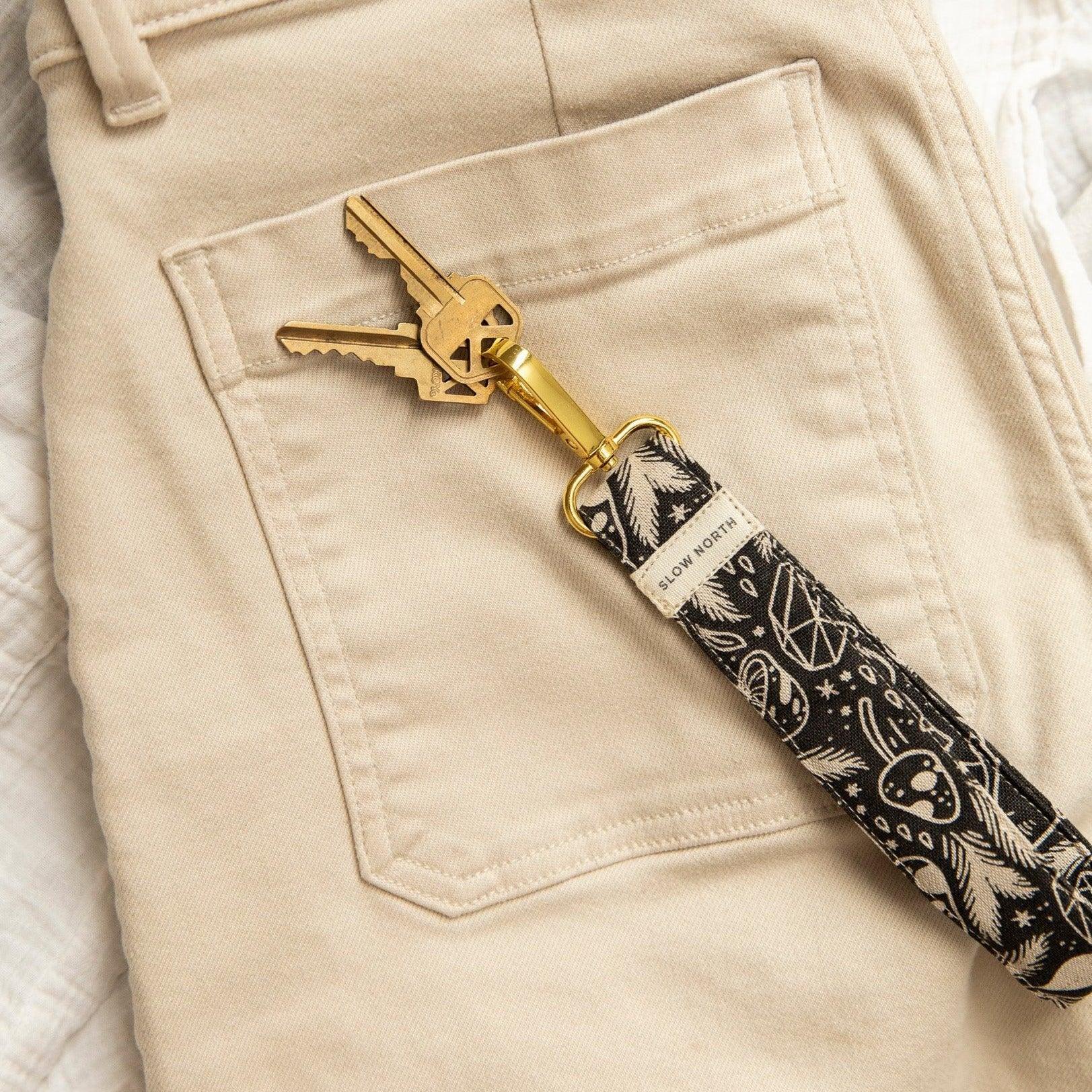 Black and white mystical mushroom wristlet keychain clipped to beige pants pocket with gold keys