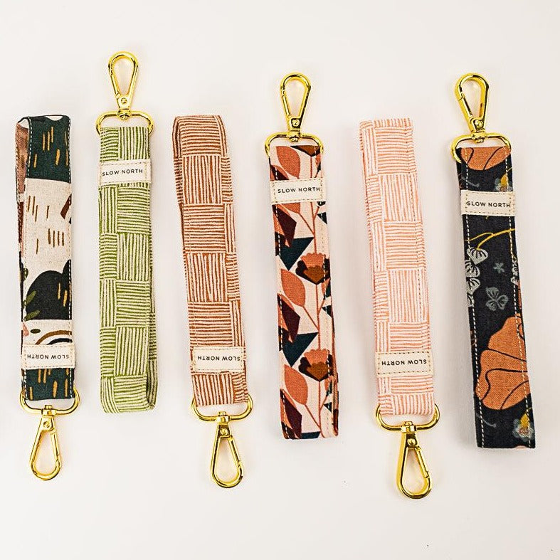 Six colorful fabric wristlet keychains with gold clasps laid out on white background
