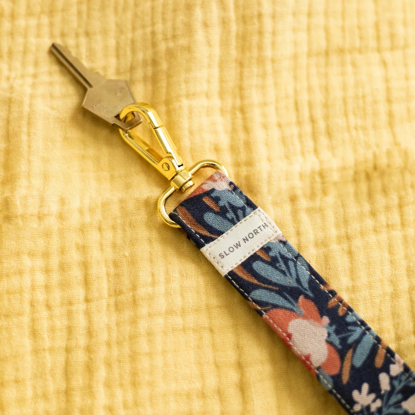 Floral wristlet keychain with gold hardware on yellow fabric, Slow North label visible
