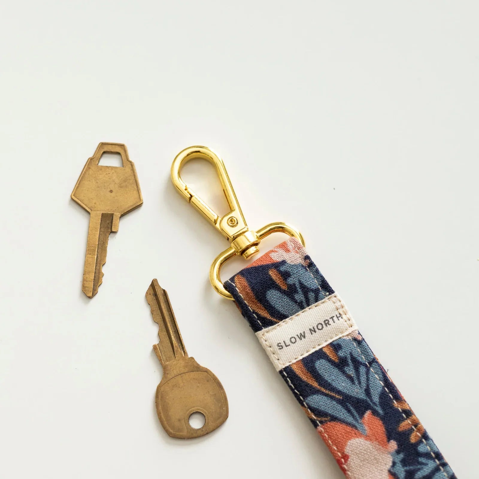 Floral fabric wristlet keychain with gold clasp and two brass keys on white background