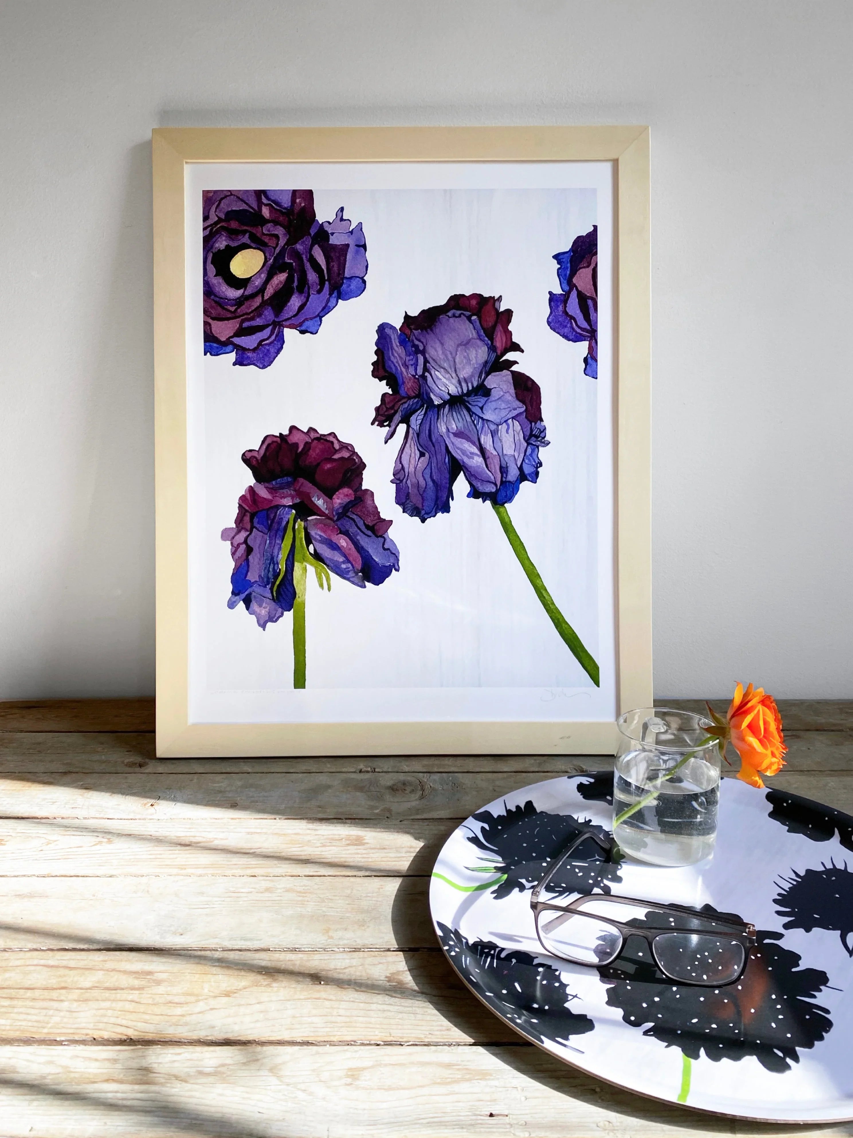 Framed floral artwork with purple flowers on wall, black floral serving tray with orange rose and glasses