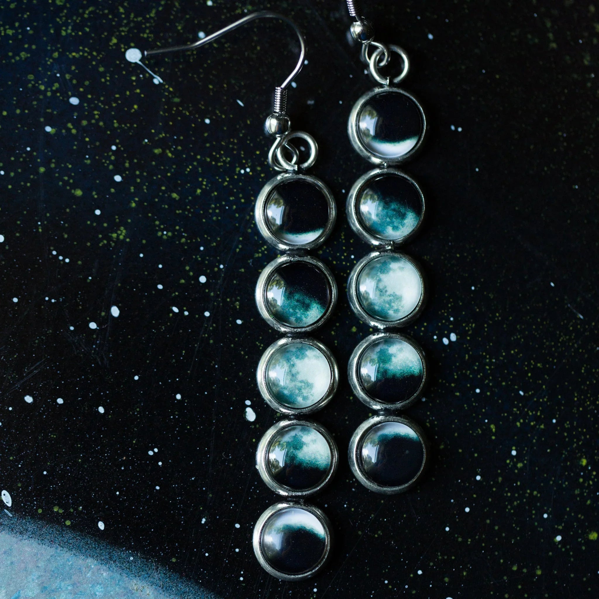 Silver earrings with moon phase designs on a black starry background