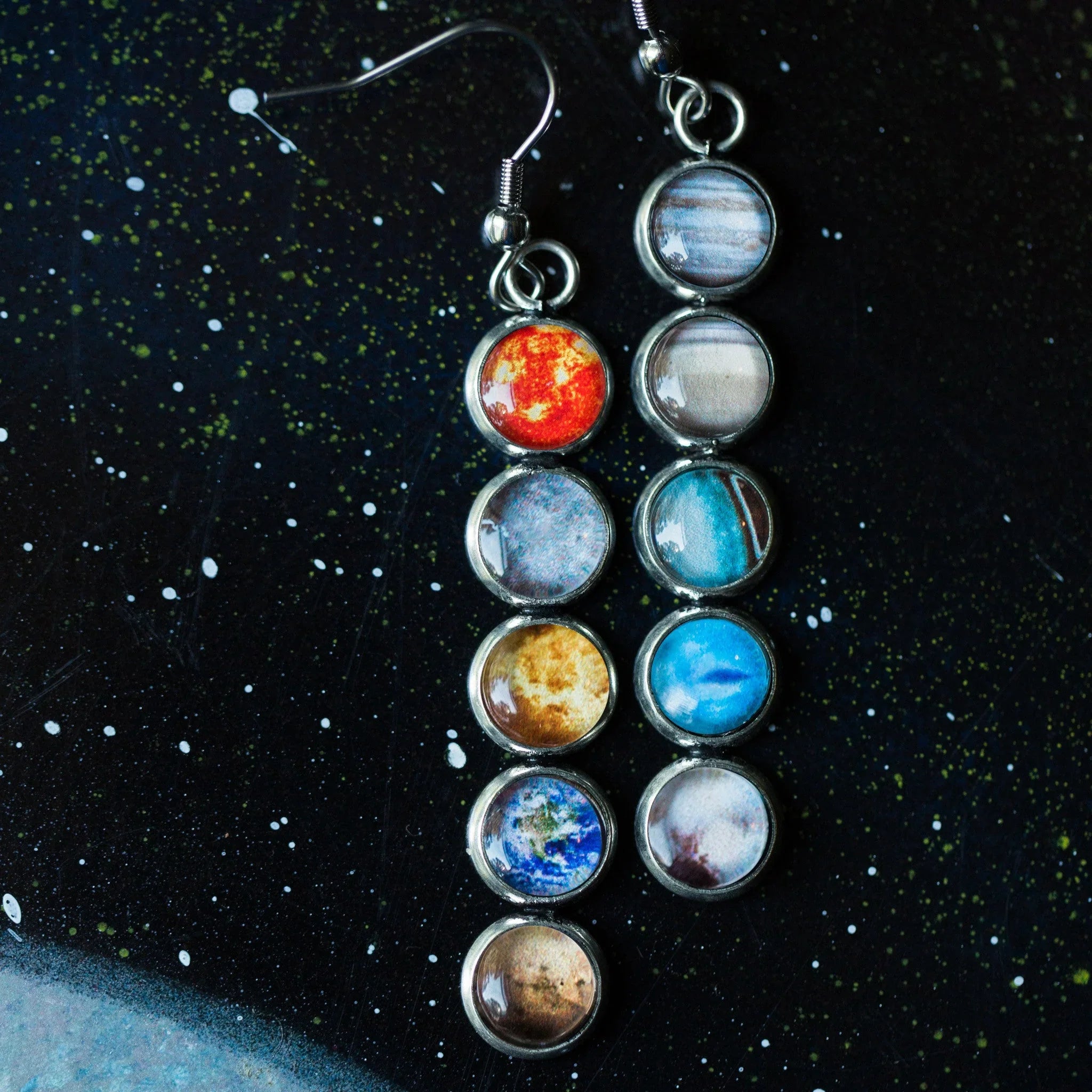 Silver earrings with seven planet images against a starry black background