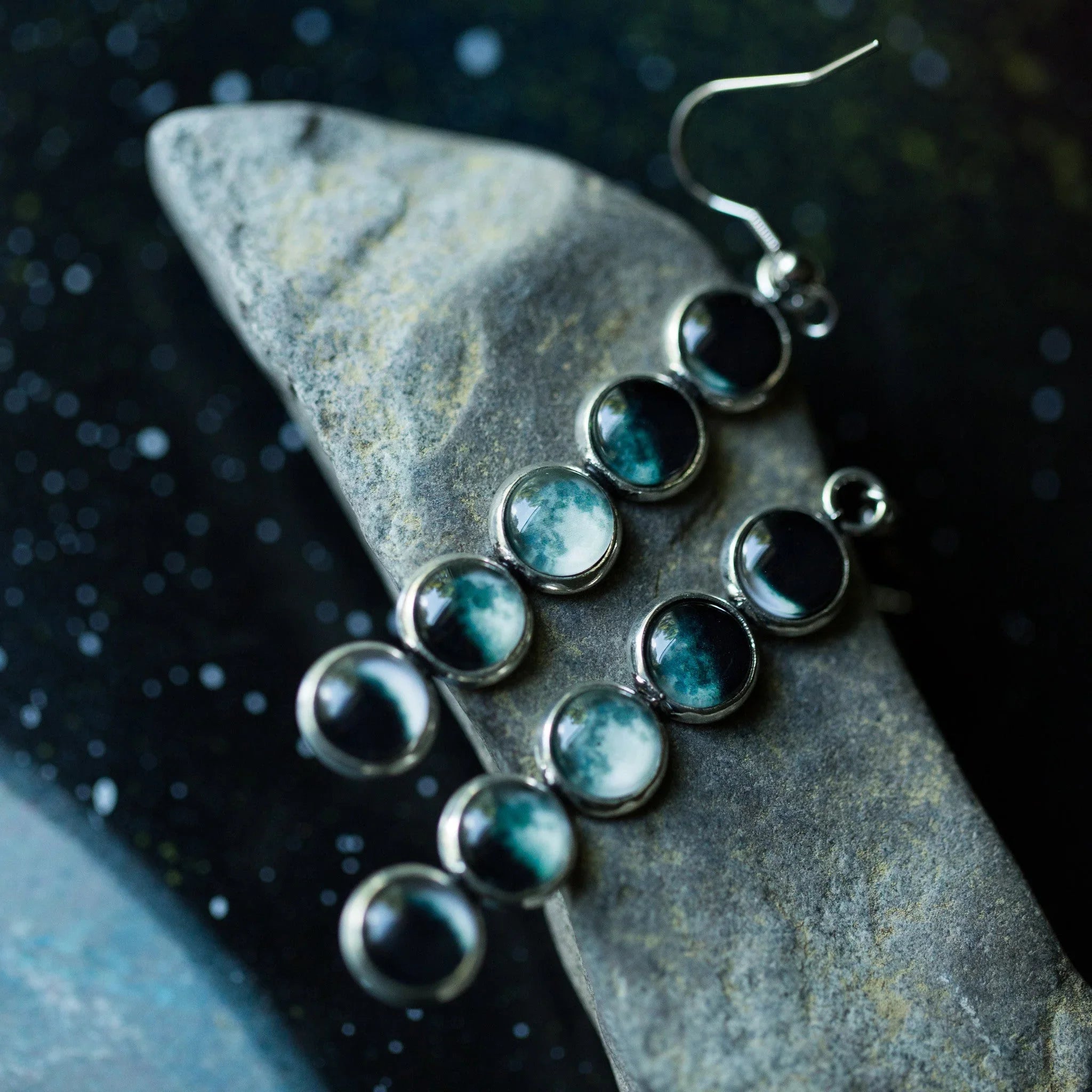 Silver dangle earrings with round blue and white stones on textured gray stone background