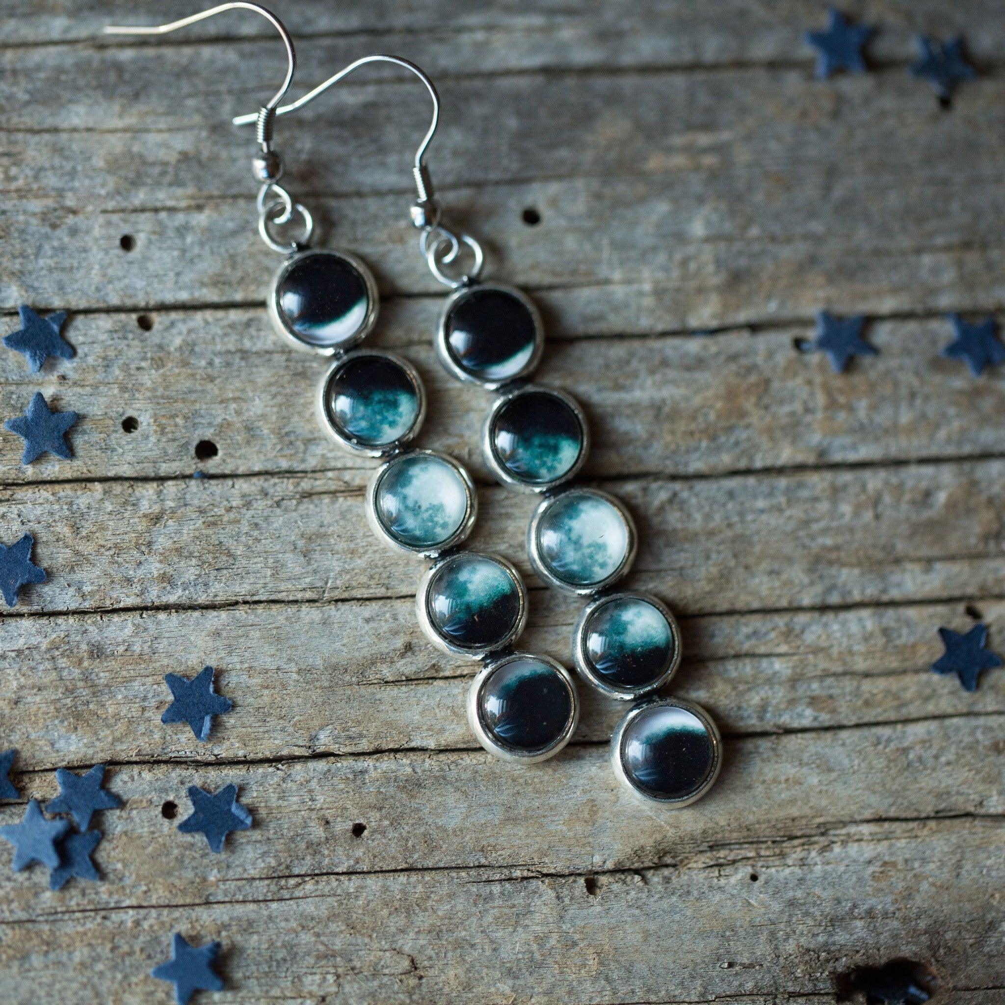 Silver earrings with glass dome phases of the moon design on rustic wooden background with blue star confetti