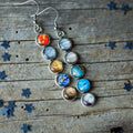 Silver dangle earrings featuring planets themed glass cabochons on rustic wood background with star confetti