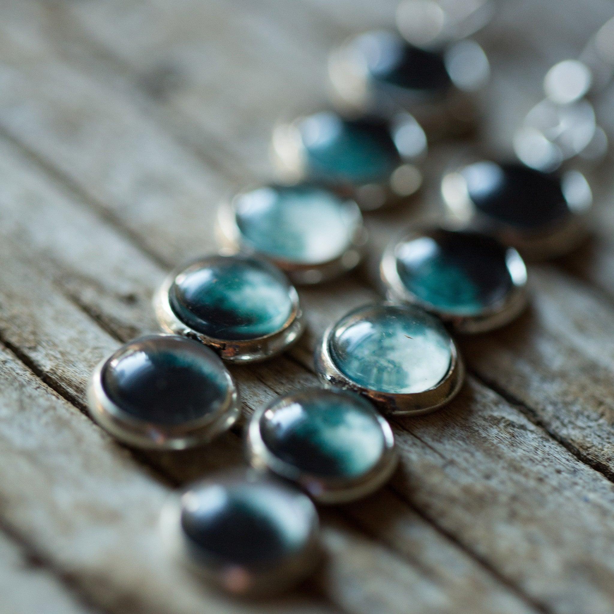 Close-up of blue and black glass cabochons with metallic bases on wooden surface