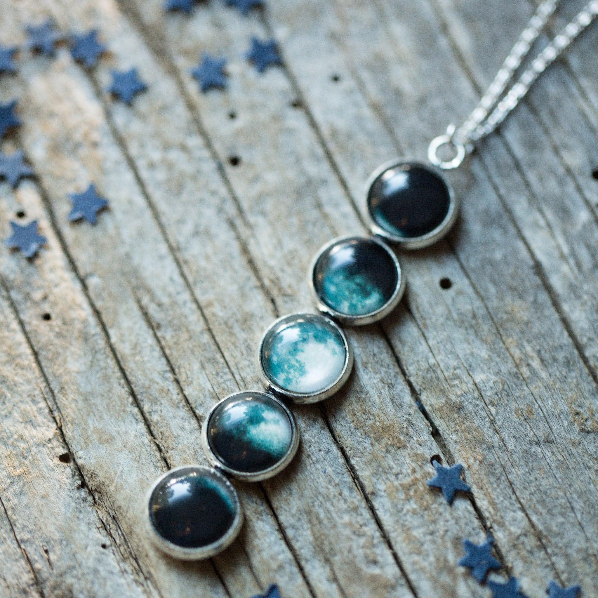 Moon phase pendant necklace with five silver-framed moon images on rustic wooden background