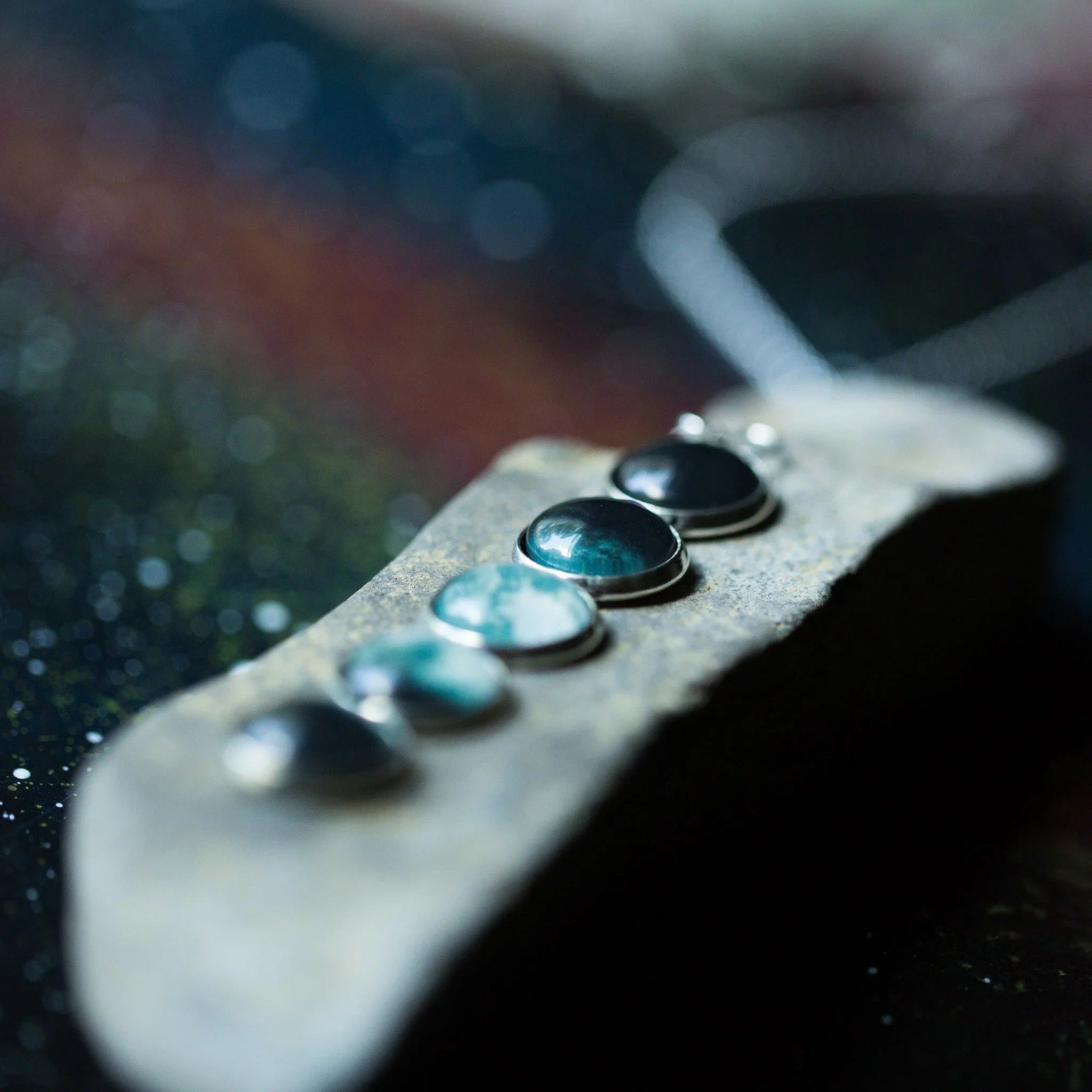 Close-up of a necklace with five round stones in different shades of green and blue on a textured pendant