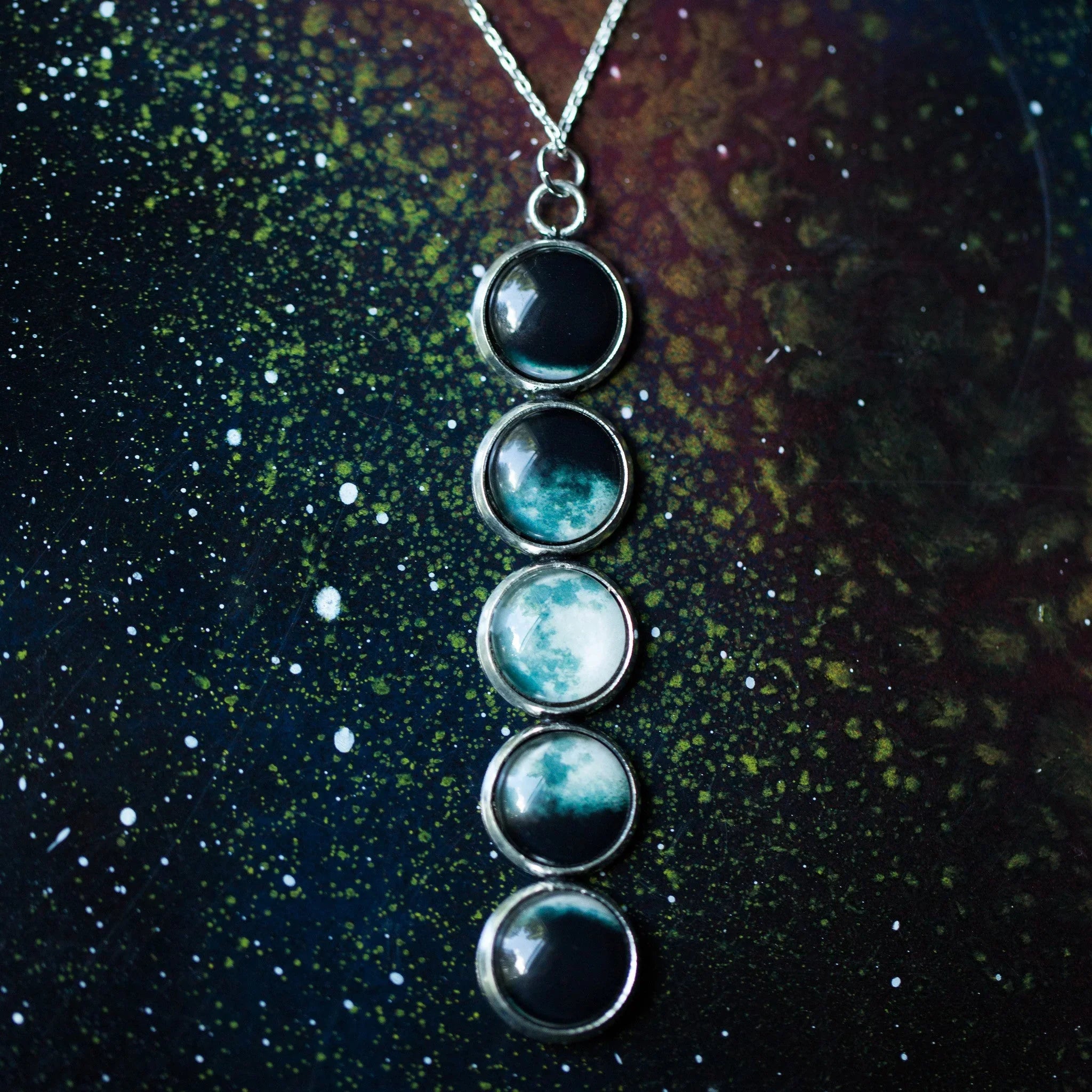 Silver necklace pendant featuring five moon phase glass cabochons on starry cosmic background