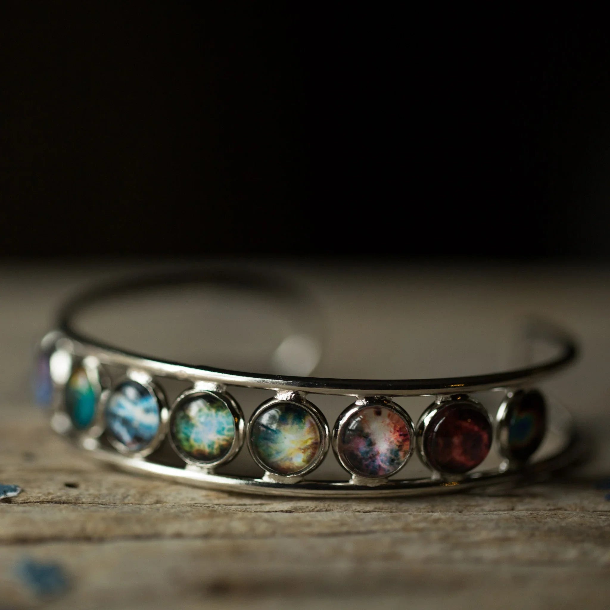 Silver cosmic bracelet with colorful galaxy cabochons on rustic wood, Qu!rk Boutique jewelry