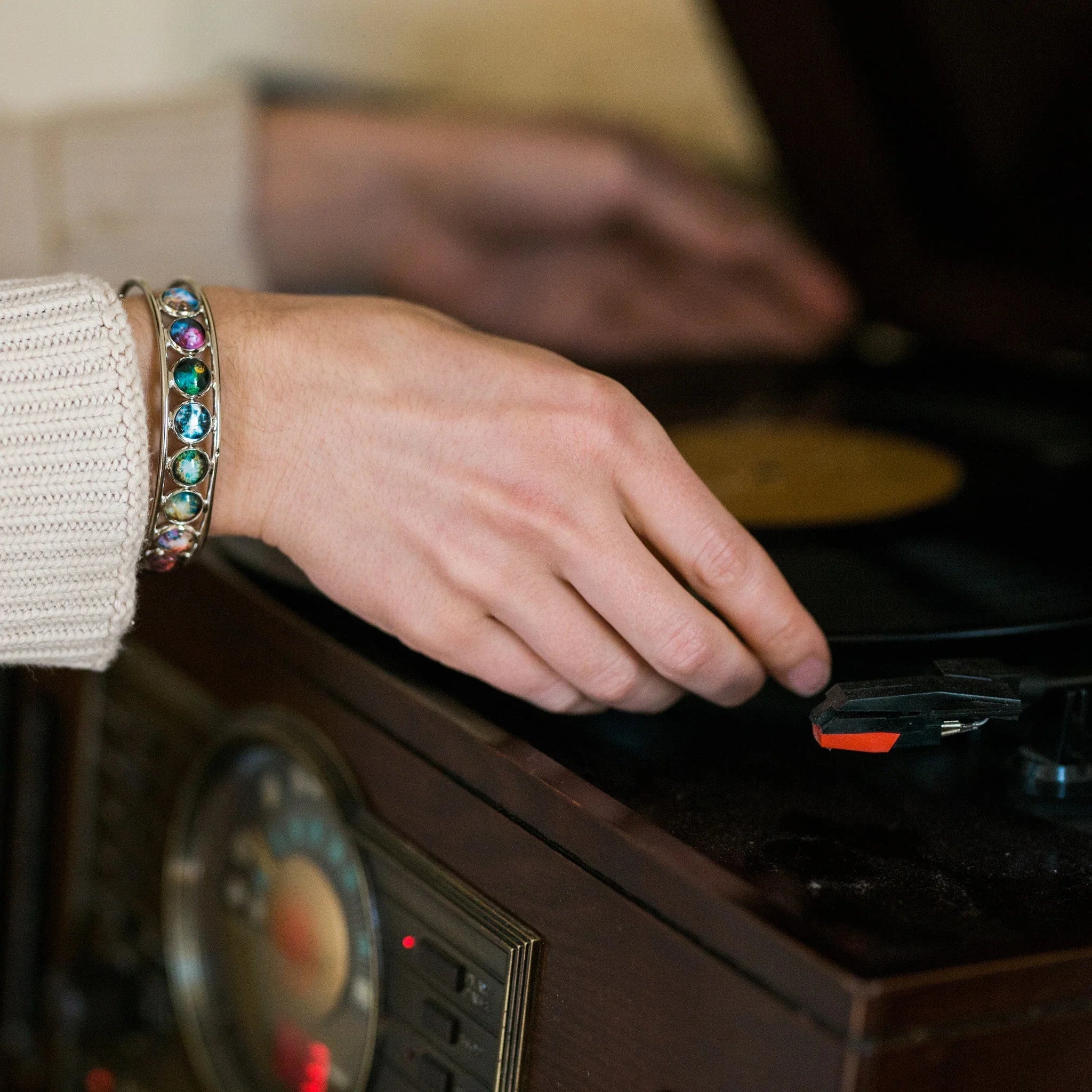 Hand with colorful gemstone bracelet on a vintage record player, cozy sweater detail