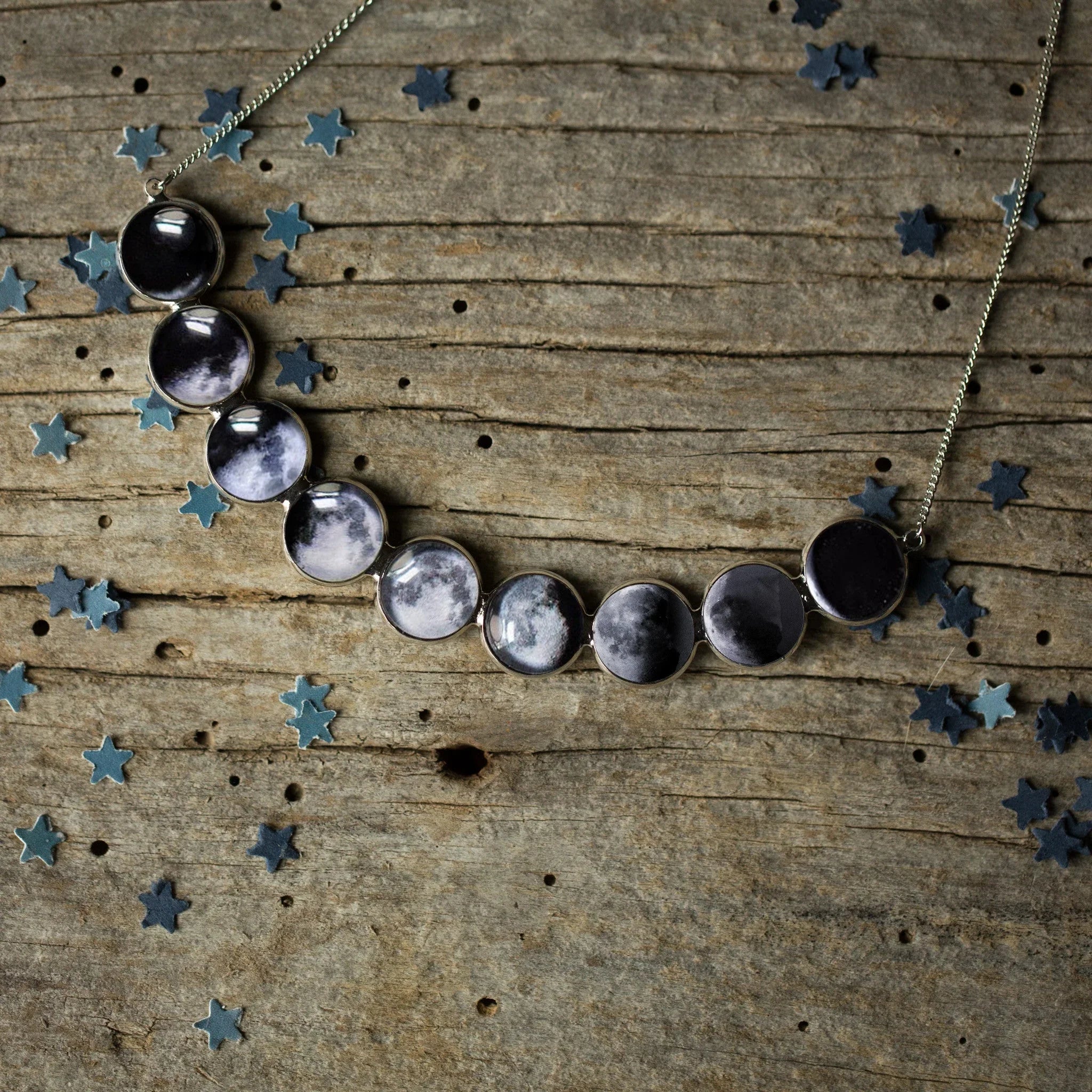 Silver necklace featuring phases of the moon pendants on rustic wooden background with star confetti