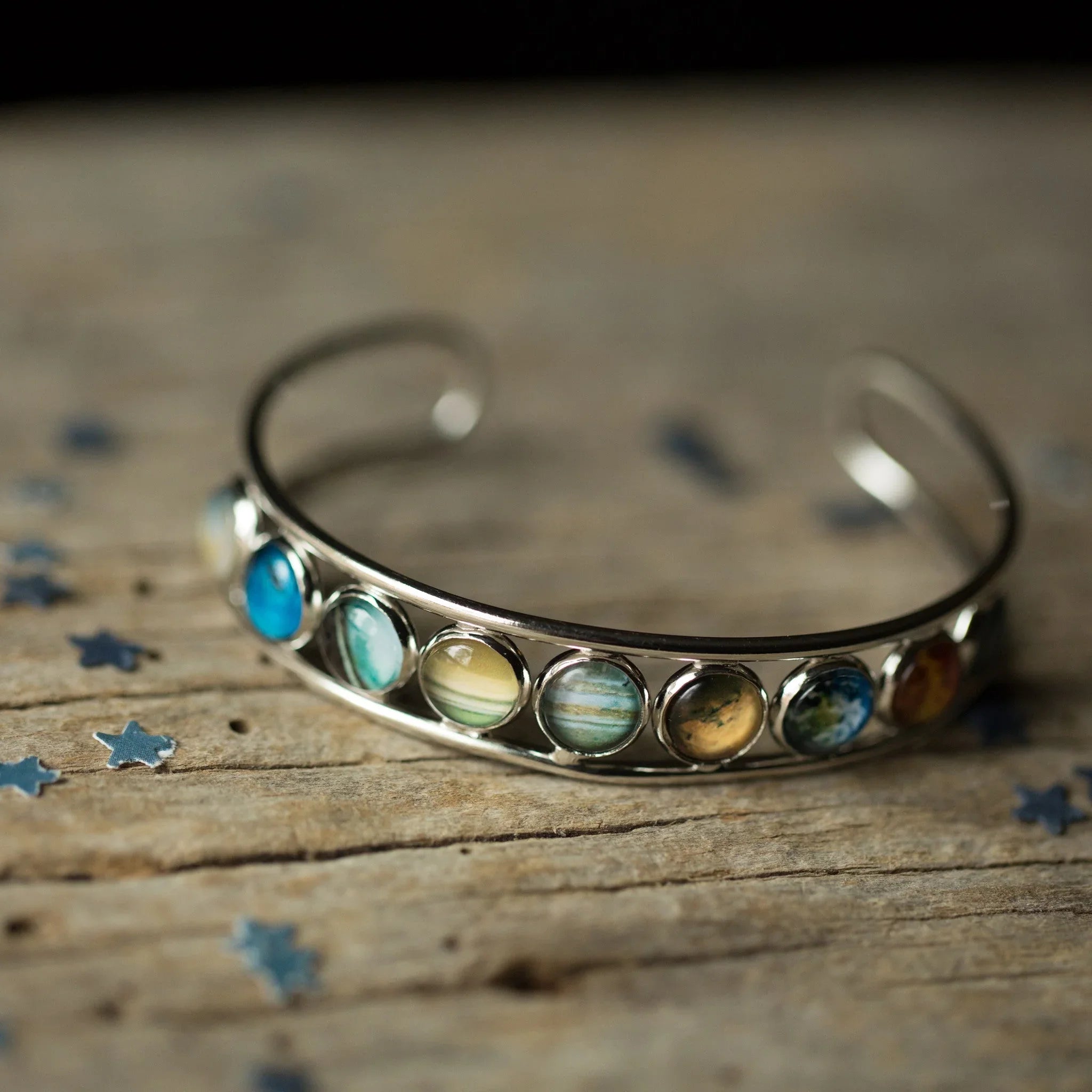 Silver cuff bracelet with round planet gemstones on rustic wooden surface with blue star confetti