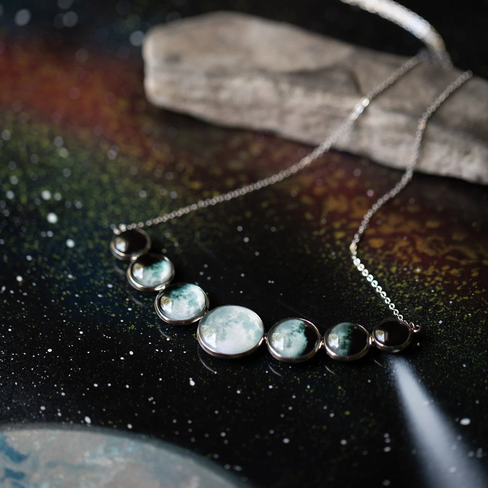 Silver necklace with seven moon phase pendants on a starry galaxy background