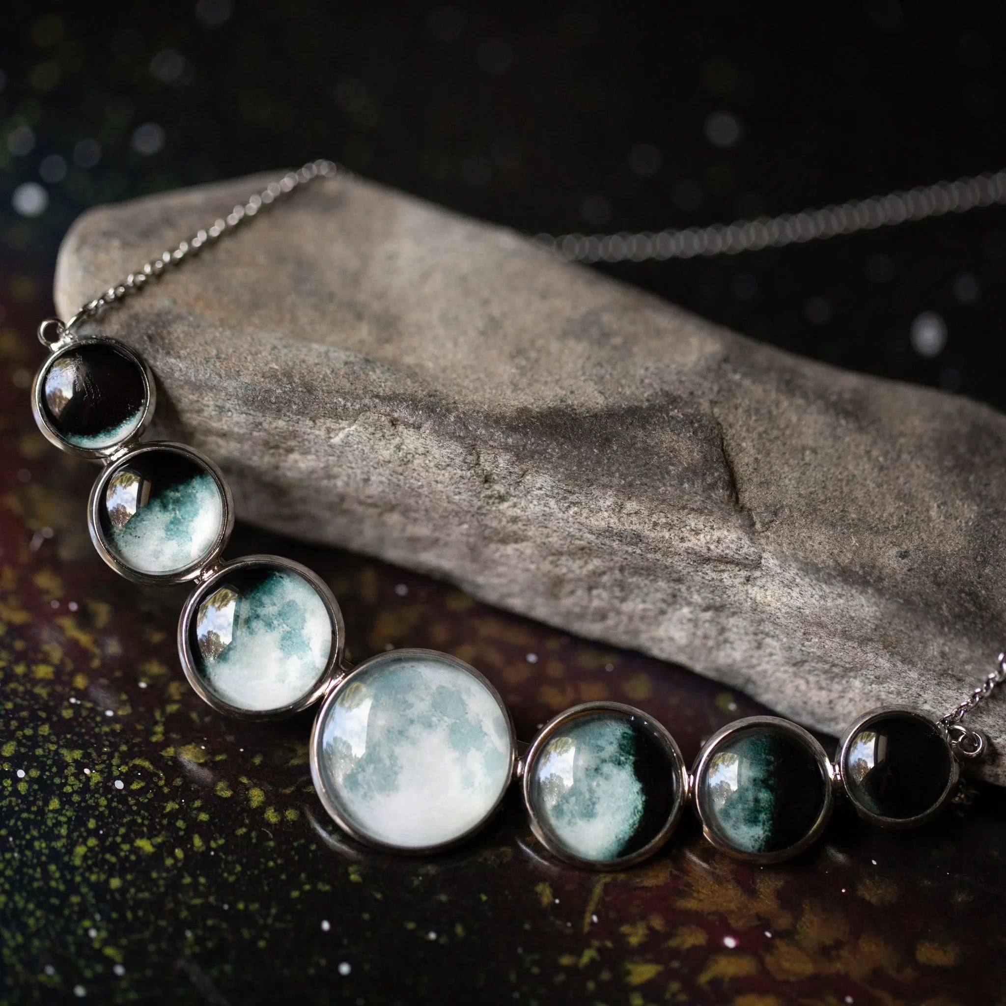 Moon phase necklace with seven circular pendants on silver chain displayed on textured stone