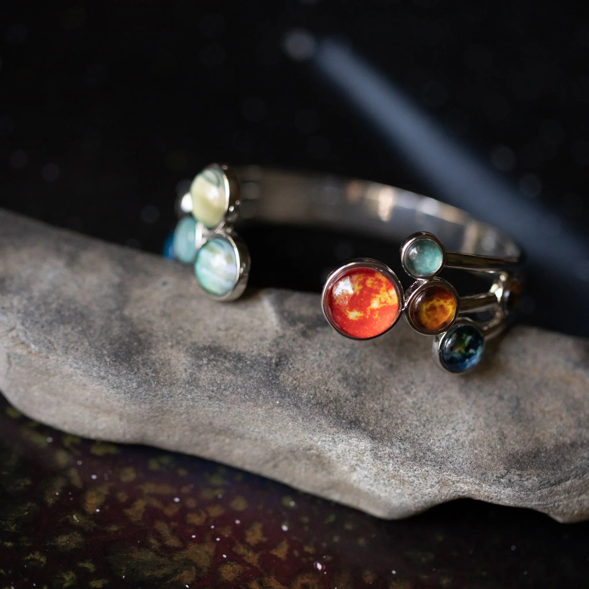 Close-up of silver bracelet with colorful planet-themed glass cabochons on stone surface