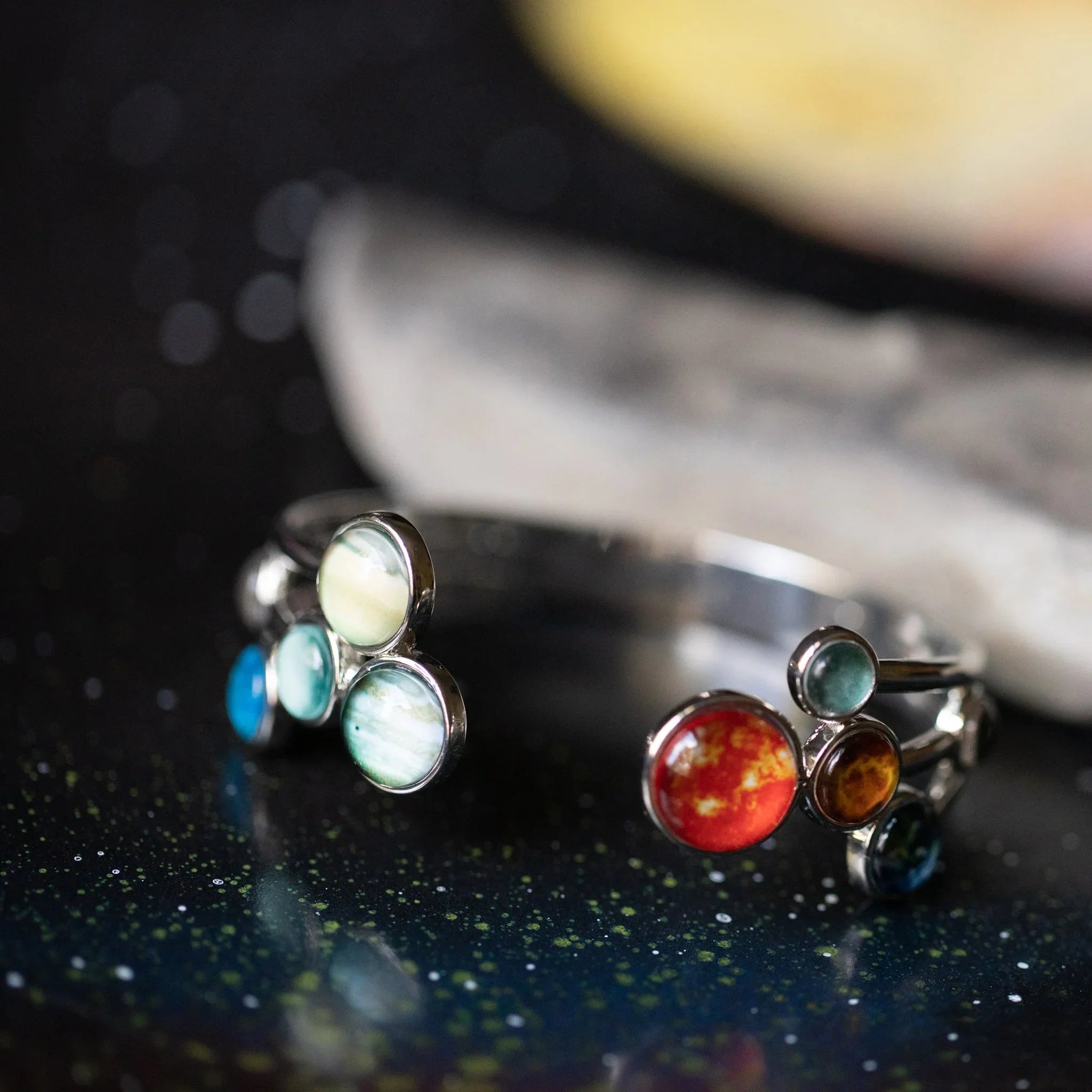 Silver rings with colorful planet-inspired stones on a starry black surface