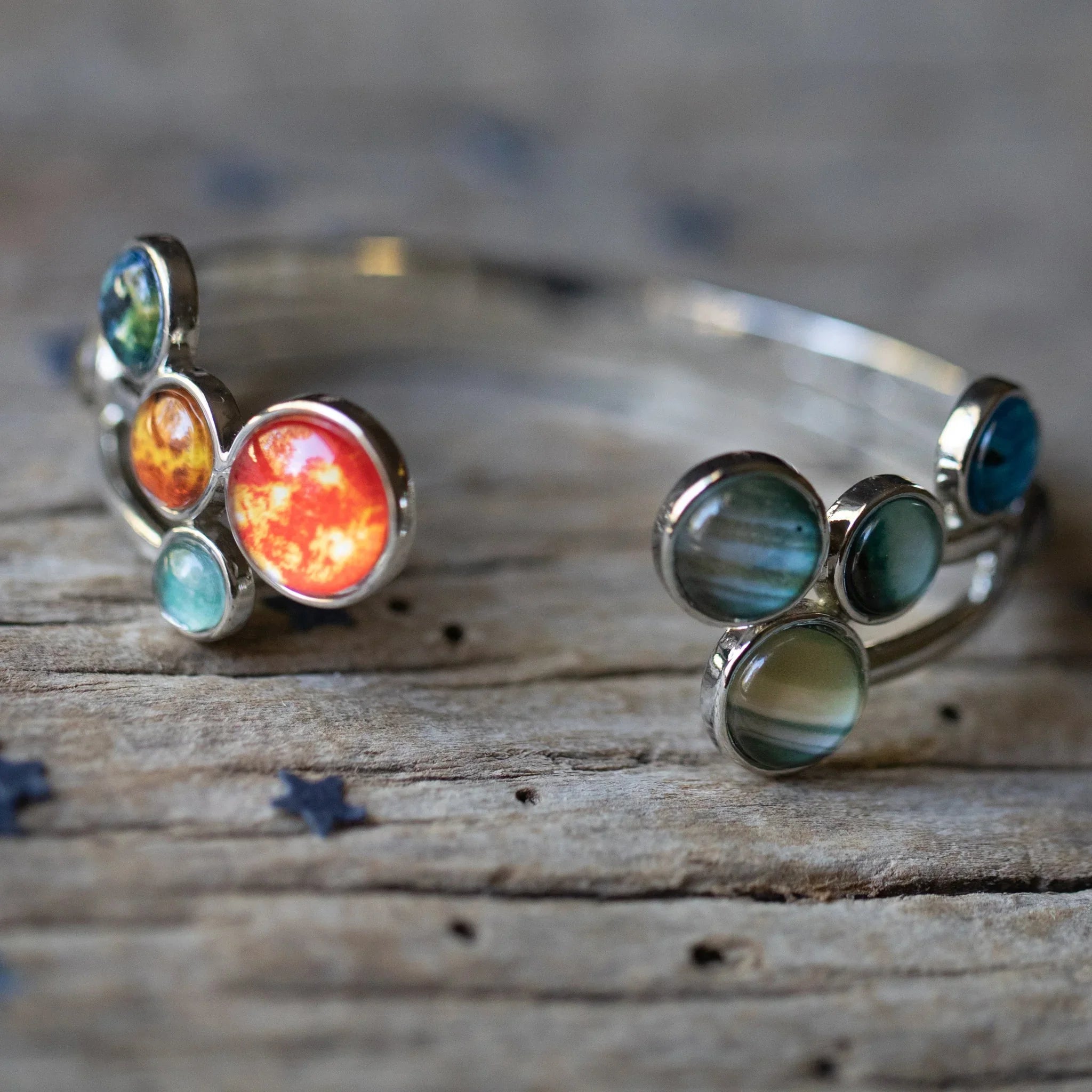 Two silver cuff bracelets with colorful round gemstone inlays on rustic wooden surface
