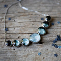 Silver necklace with seven round moon phase pendants on rustic wooden surface with star confetti