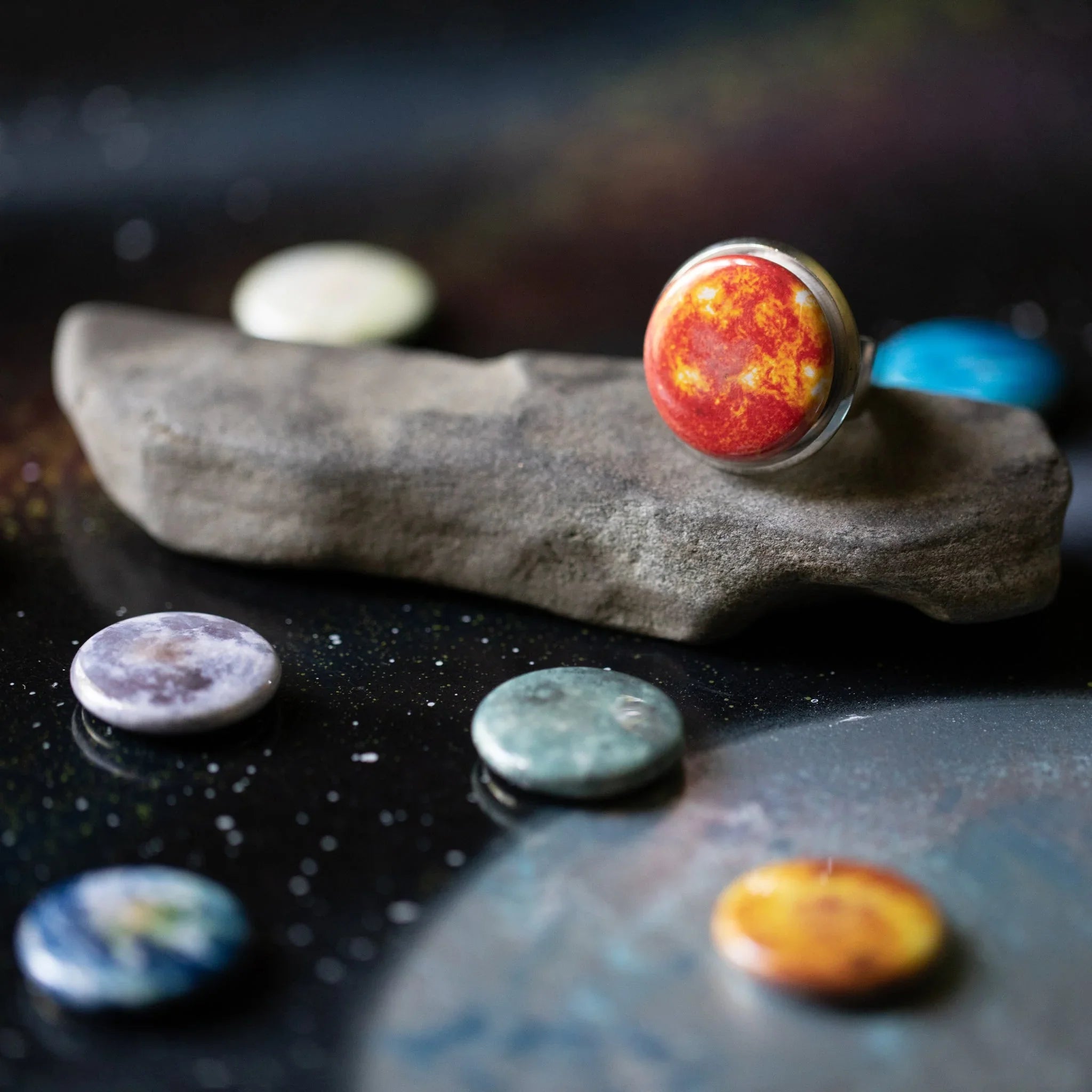Planet-themed ring on a rock surrounded by colorful planet stones on a starry surface
