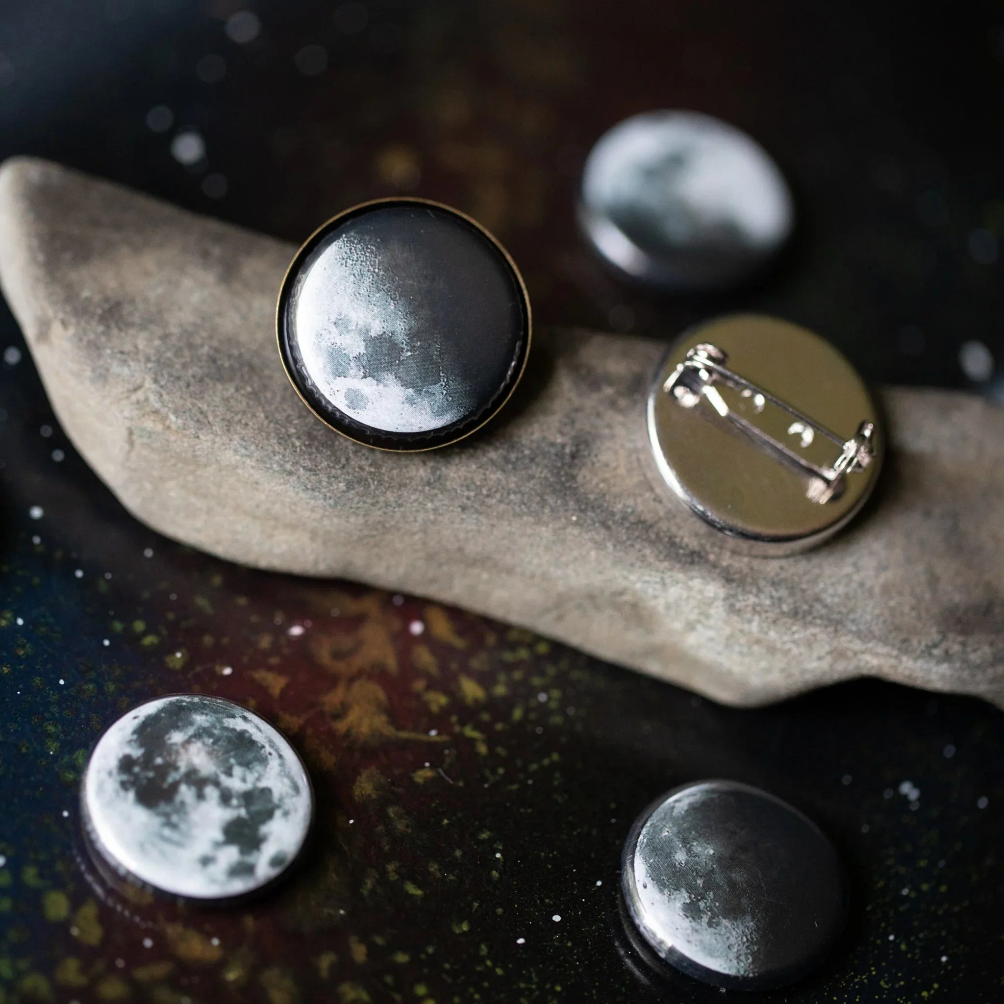 Cosmic moon phase enamel pins on stone, celestial-themed gift from Qu!rk Boutique