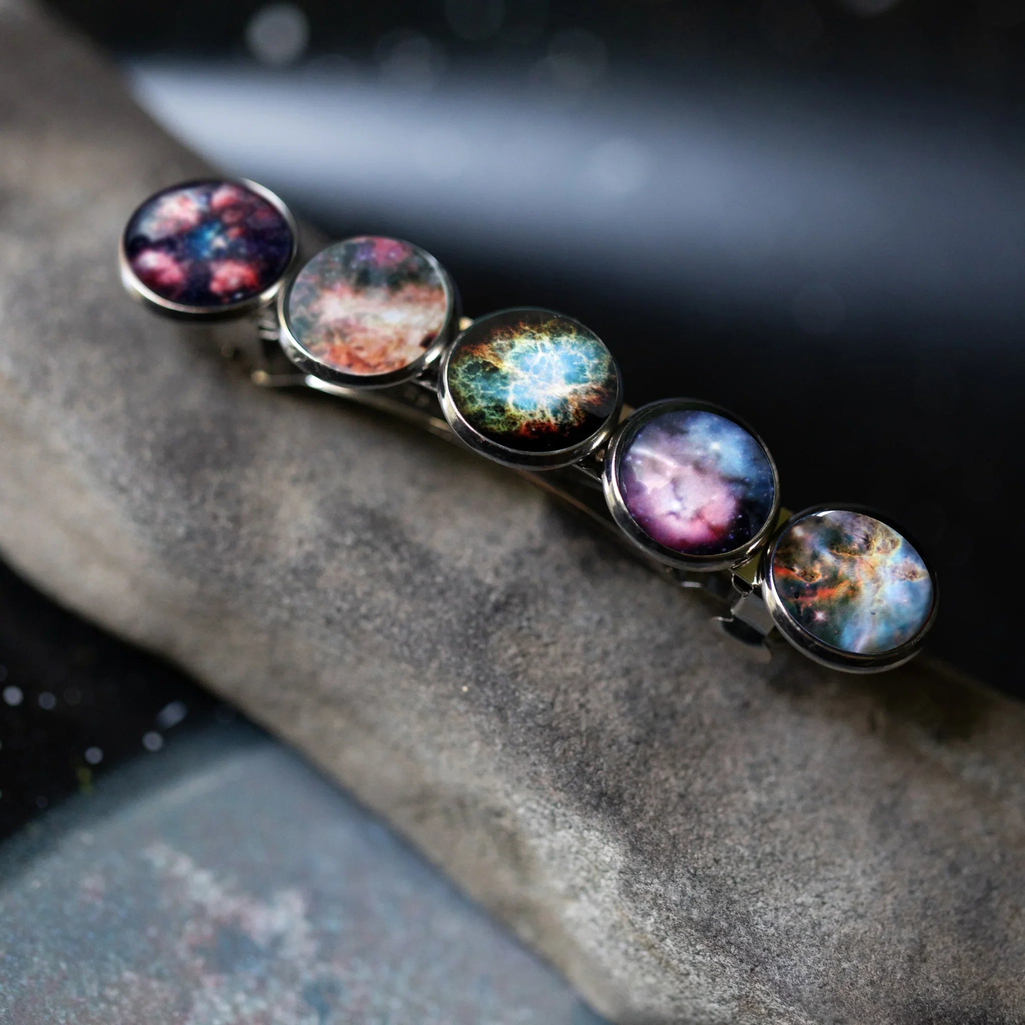 Metal hair clip with five round galaxy-themed celestial nebula designs on a textured gray surface