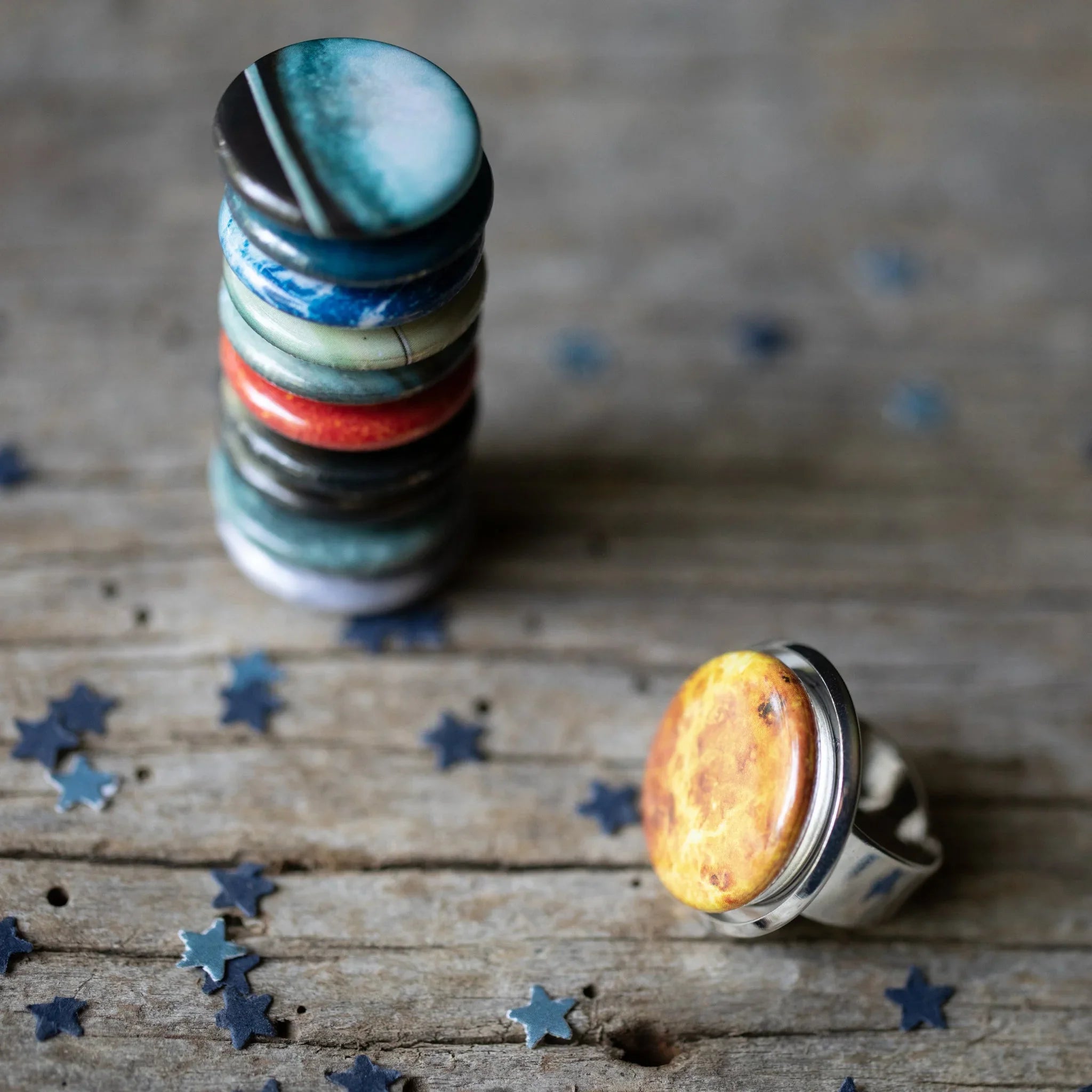 Stack of colorful round rings and single yellow-orange ring on rustic wooden surface with star-shaped confetti