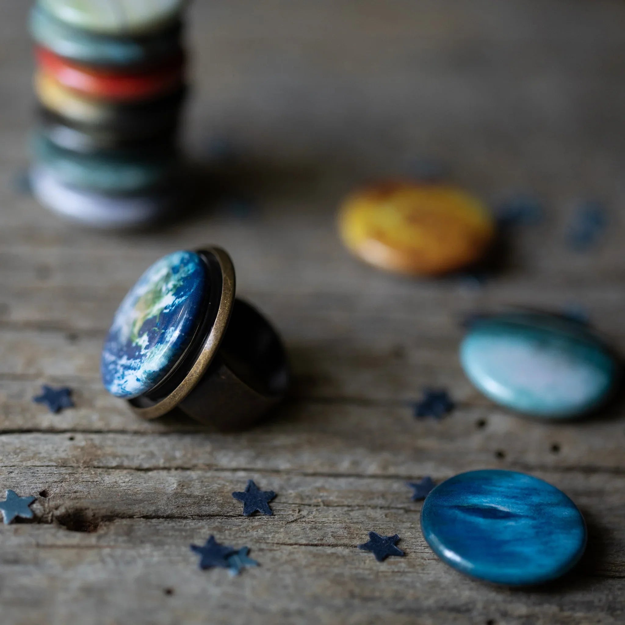 Close-up of colorful planet-themed rings and pins on rustic wooden surface with star confetti